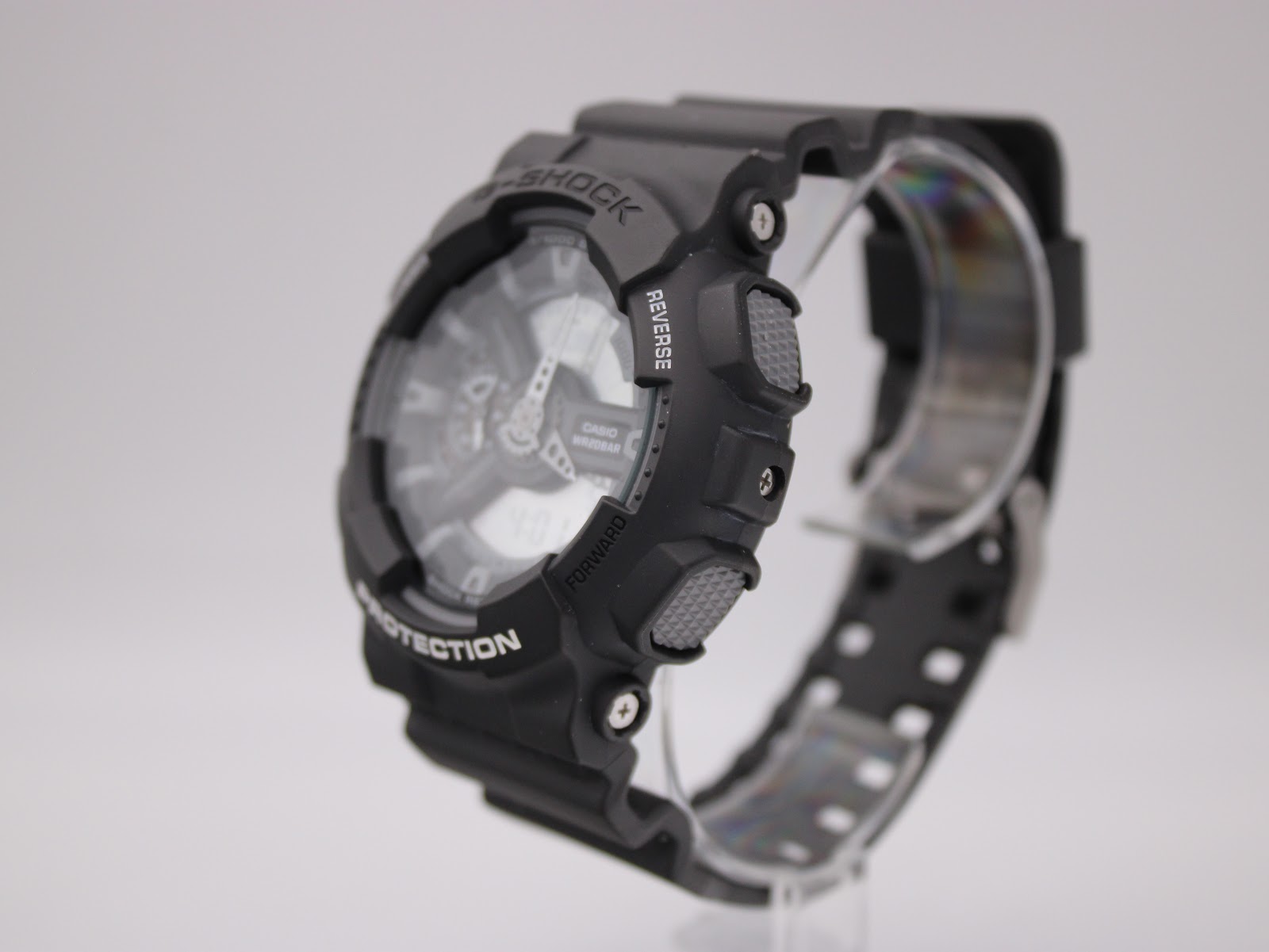 Side view of black Casio G-Shock GA-110C watch on a clear stand, showing mode buttons and textured resin case.