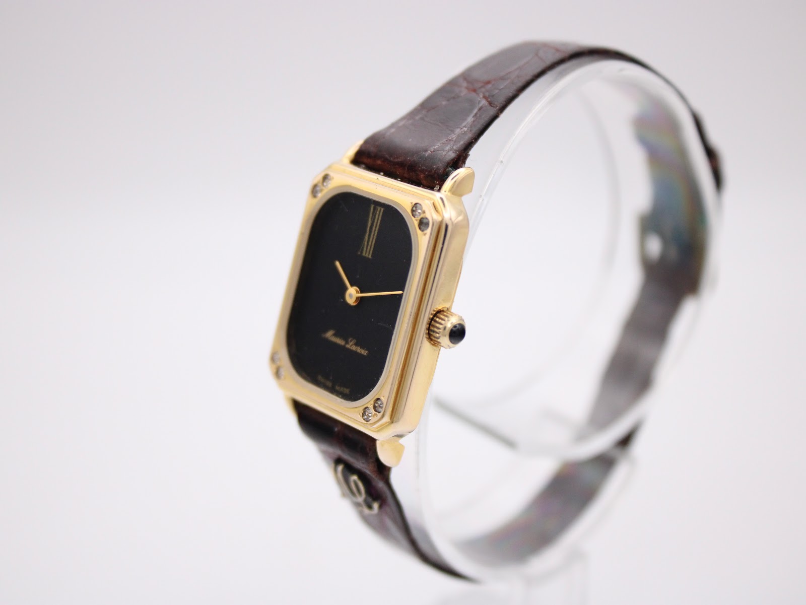 Angled view of the Maurice Lacroix watch on a clear display stand, showing the crown, side profile, and gold-tone case.