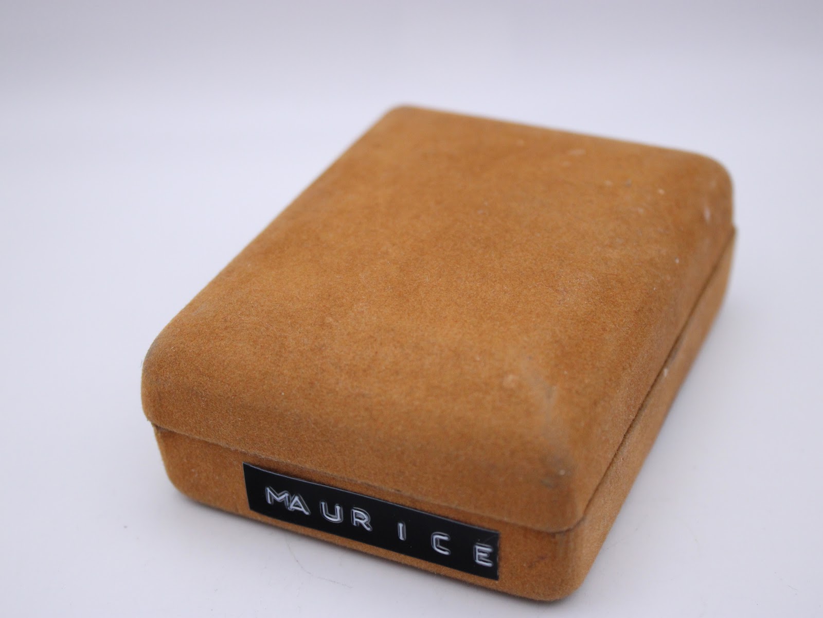 A front-facing view of the closed Maurice Lacroix watch box, made of a textured brown velvet-like material with the brand name on the front.
