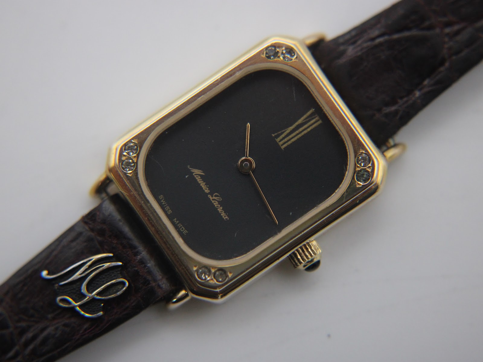 Top-down view of the watch and strap, prominently displaying the 'ML' monogram detail on the brown crocodile-effect leather strap.