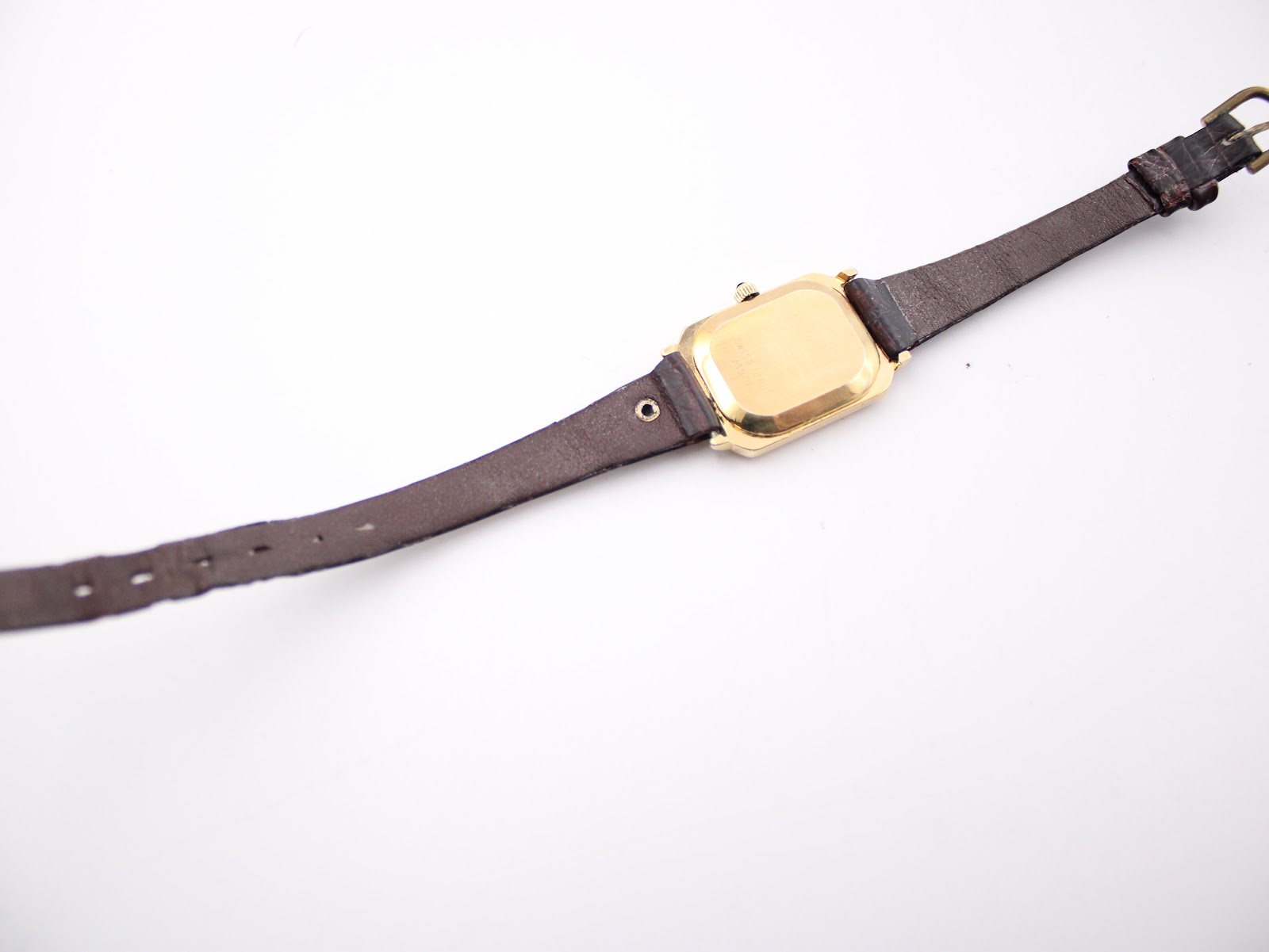 Full length back view of the watch, showing the gold-tone case back, the entire length of the leather strap, and its adjustment holes.