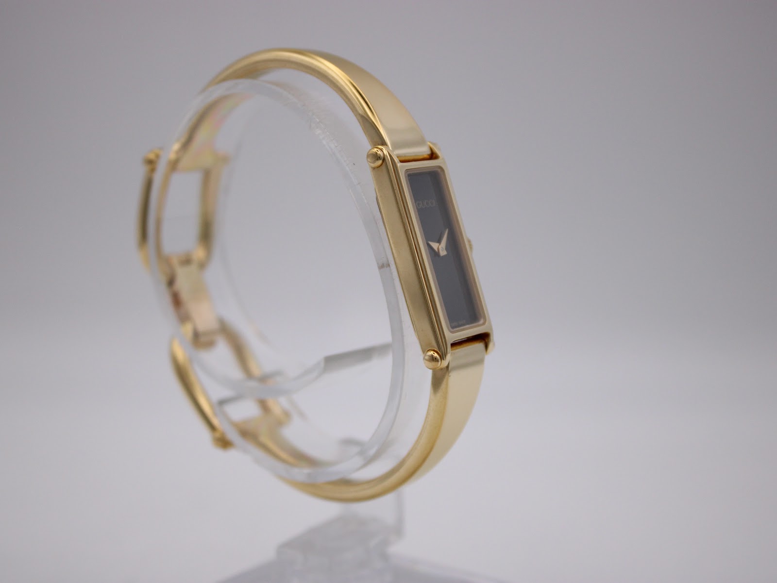 Angled view of Gucci 1500L watch on a clear display stand, showing the opposite side of the case and bracelet connection.