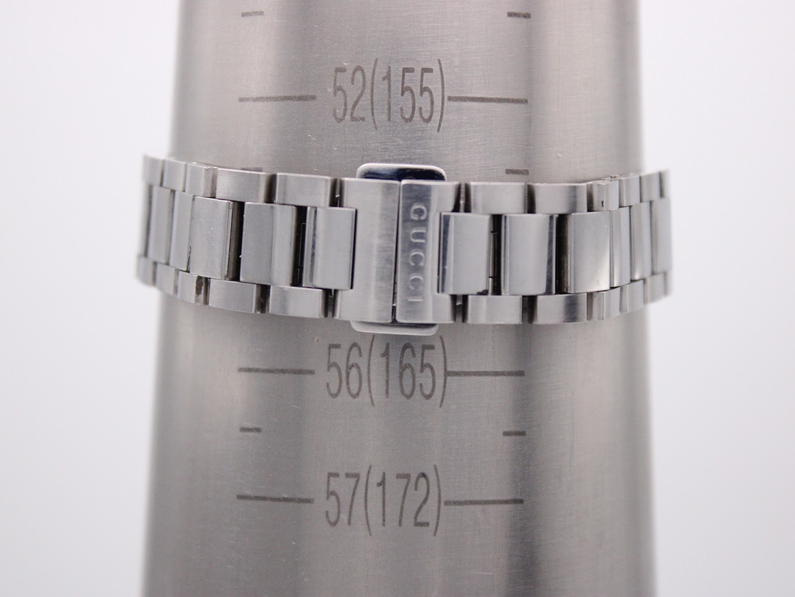 Close-up of the stainless steel bracelet with signed Gucci clasp on a wrist sizing cone, showing a measurement of approximately 155mm.