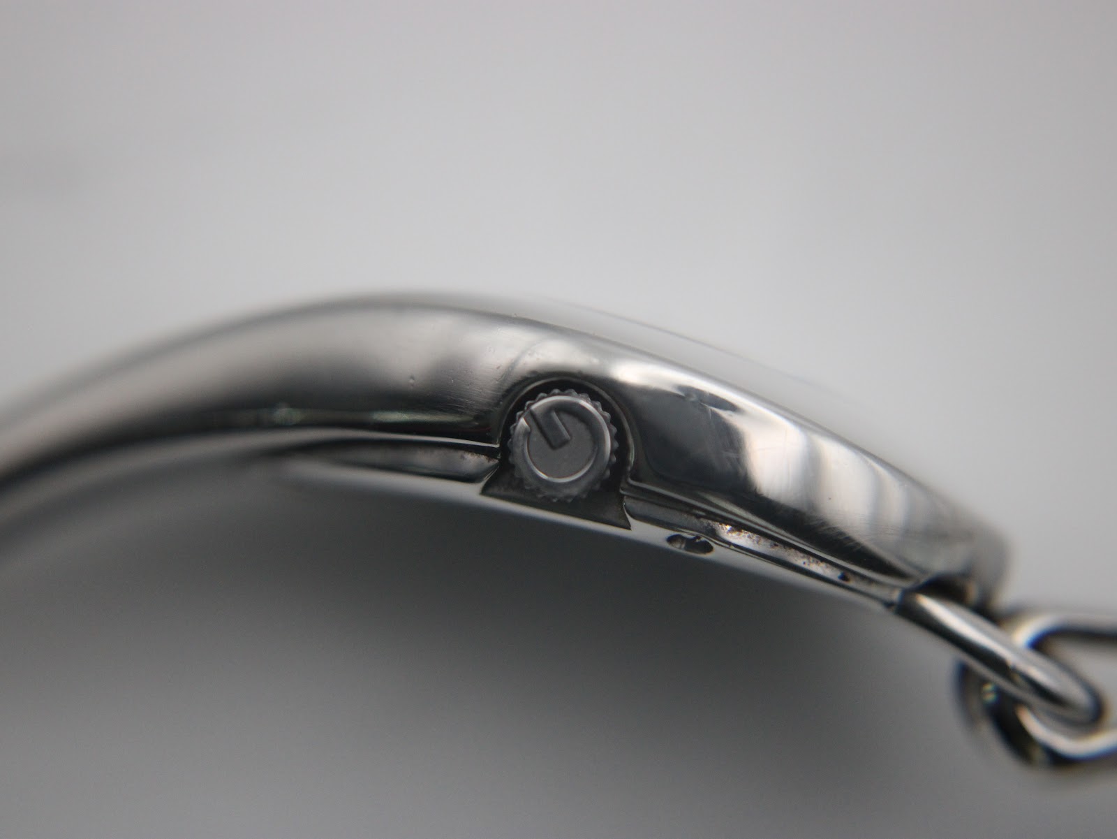 Extreme close-up of the watch crown on the side of the silver oval case.