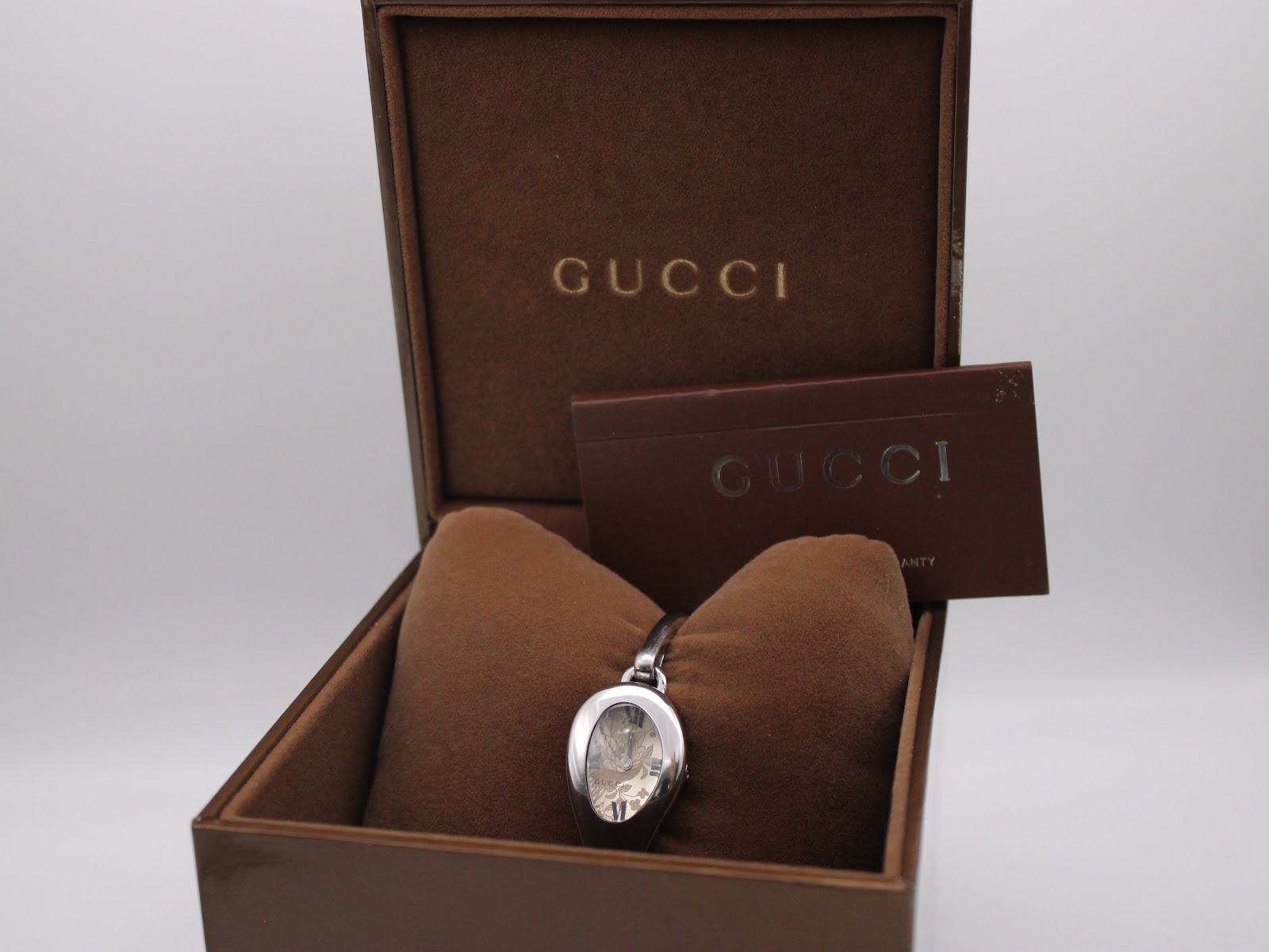 Front view of the Gucci 103 watch inside its original brown presentation box, with accompanying papers.