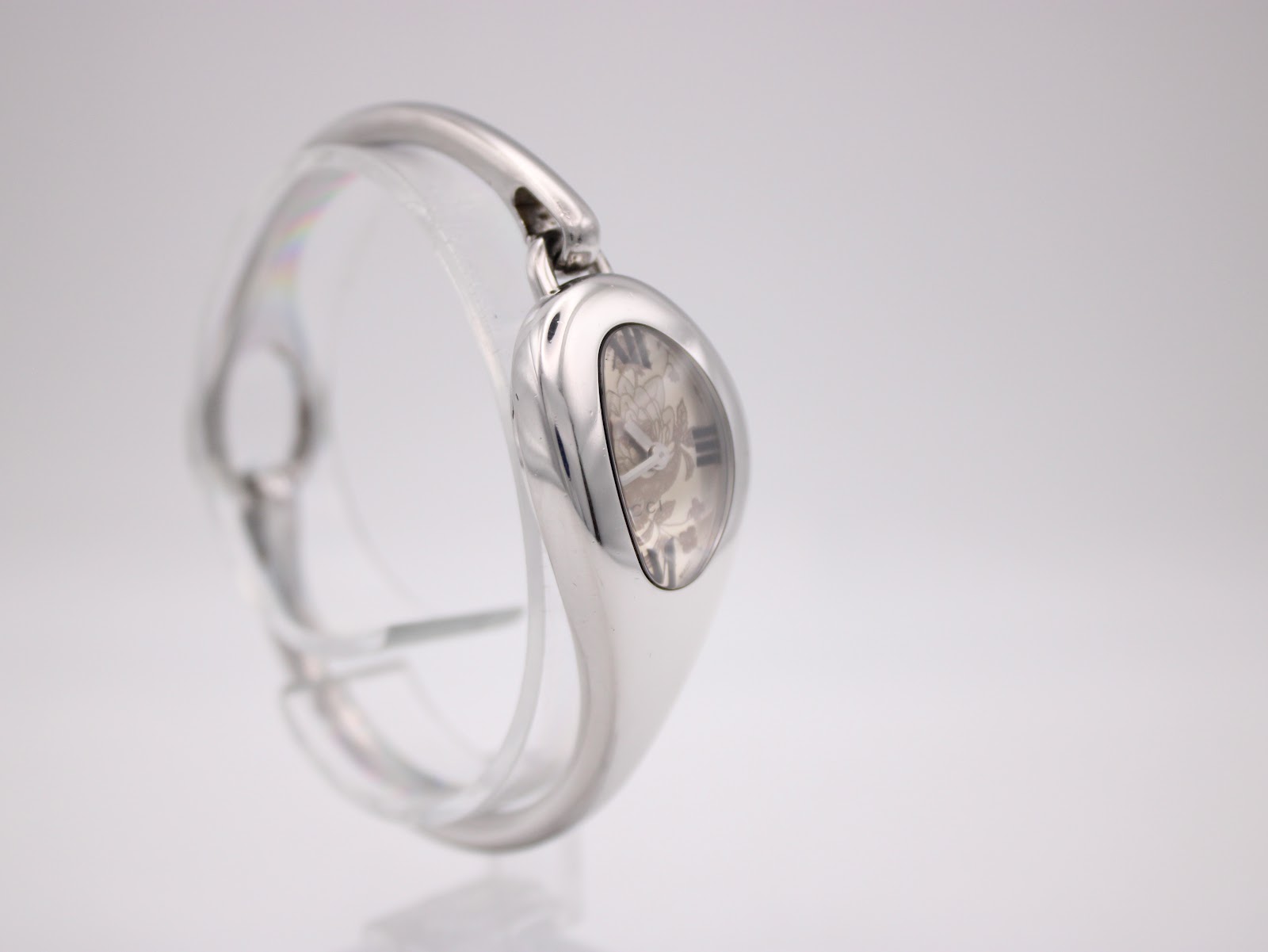 Side view of the Gucci 103 watch on a stand, highlighting the sleek, integrated bangle design and left profile.