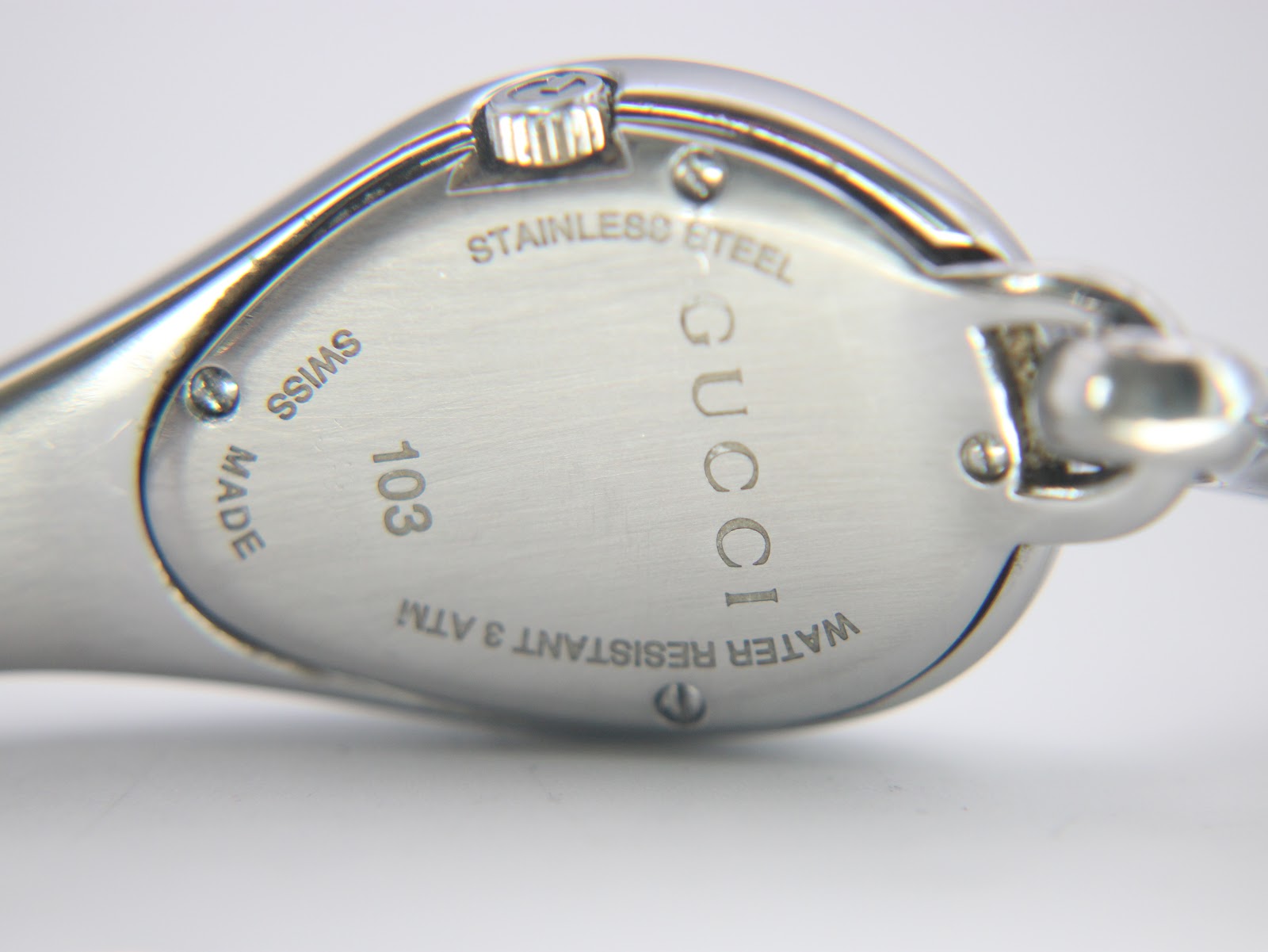 Close-up of the watch case back, engraved with 'STAINLESS STEEL', 'GUCCI', '103', 'SWISS MADE', and 'WATER RESISTANT 3 ATM'.