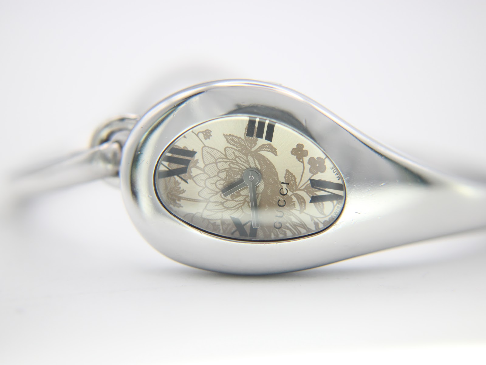 Extreme close-up of the Gucci 103 watch dial, clearly showing the cream floral pattern, black roman numerals, and 'GUCCI' branding.