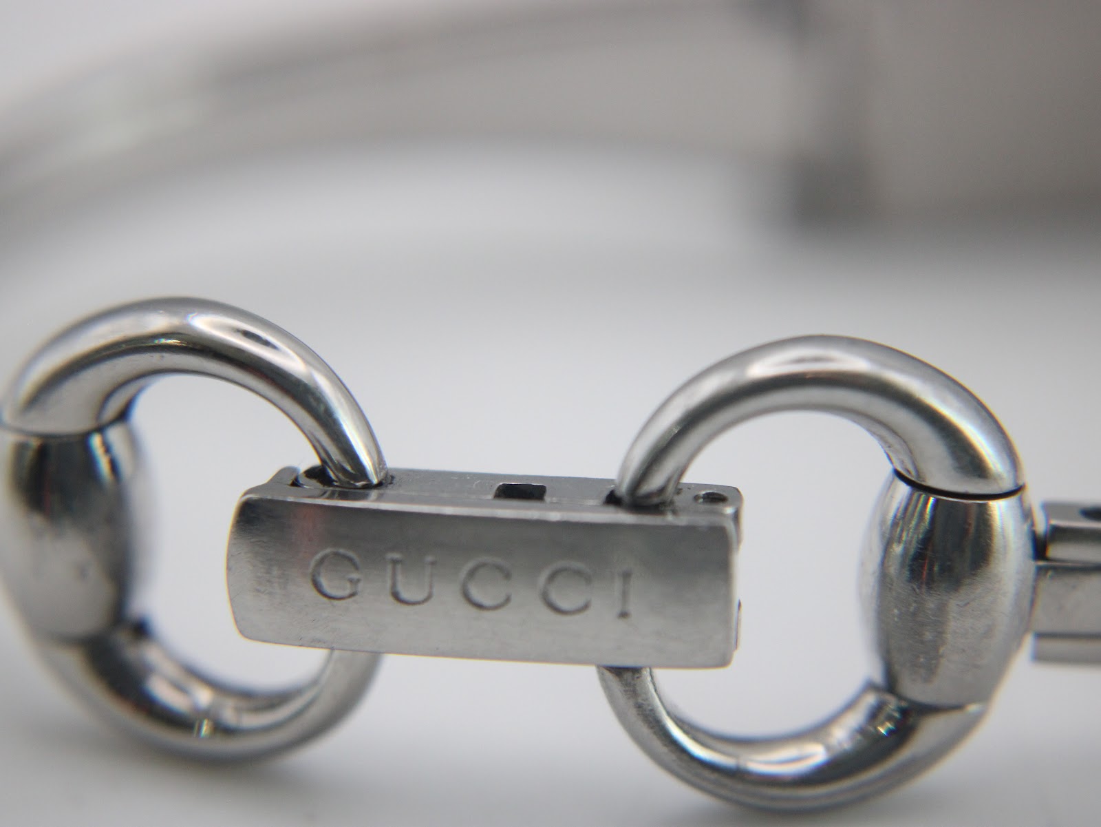 Macro shot of the integrated bracelet's push-button deployant clasp, with 'GUCCI' engraved on the buckle.