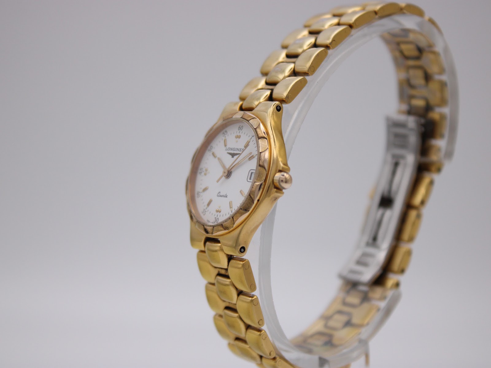 Angled side view of the Longines Conquest watch on a clear display stand, showing the bracelet.