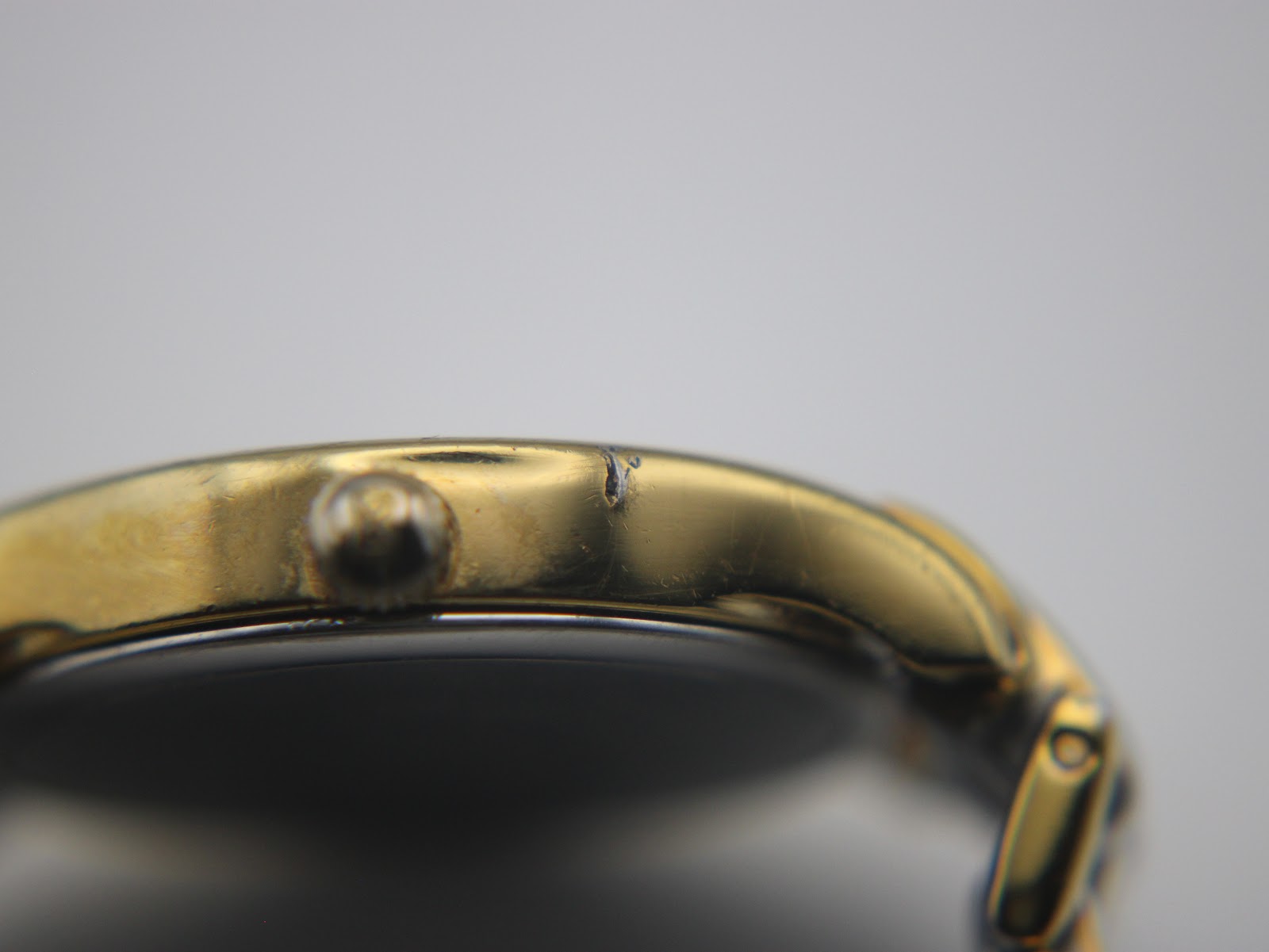 Extreme close-up of a ding or chip on the gold-tone plating on the side of the watch case, near the crown.