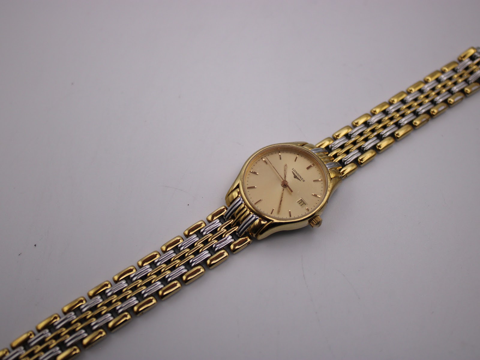 Long shot of the Longines Lyre watch and its full two-tone stainless steel bracelet on a white surface.