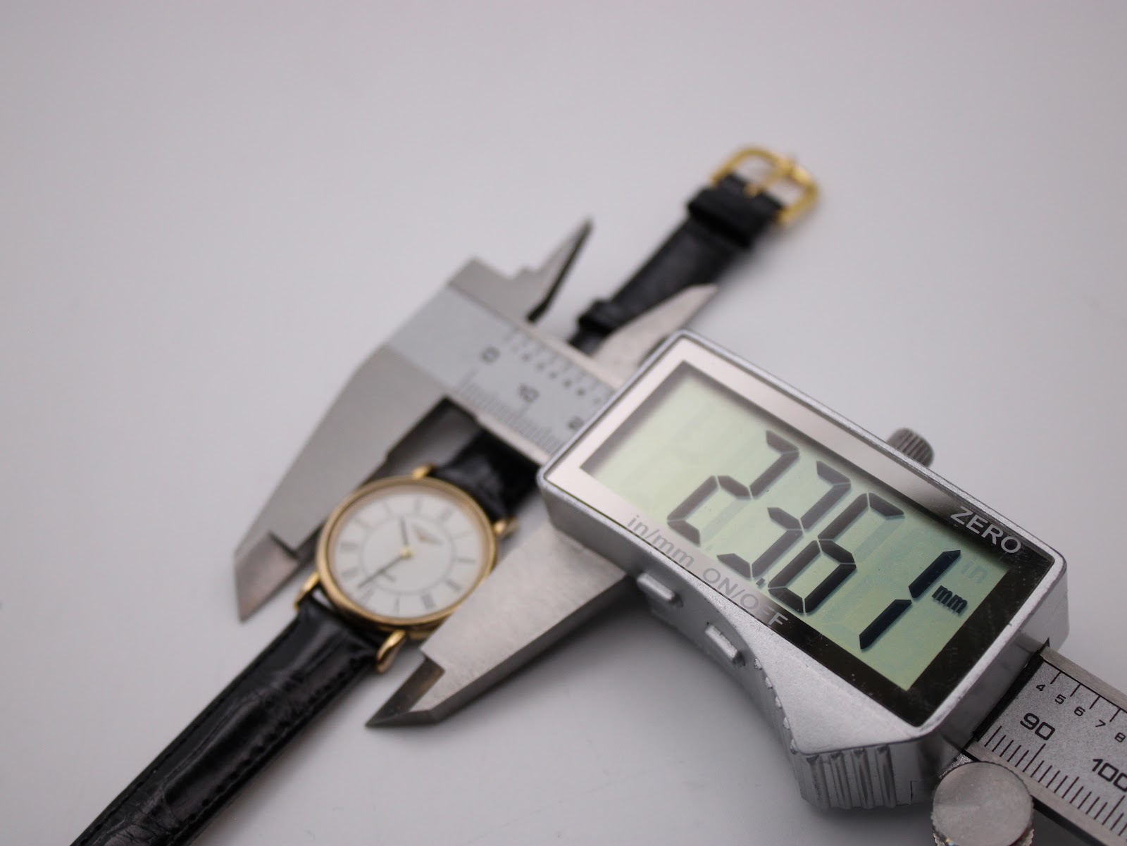 Digital caliper measuring the Longines watch case diameter, showing a precise reading of 23.61mm.