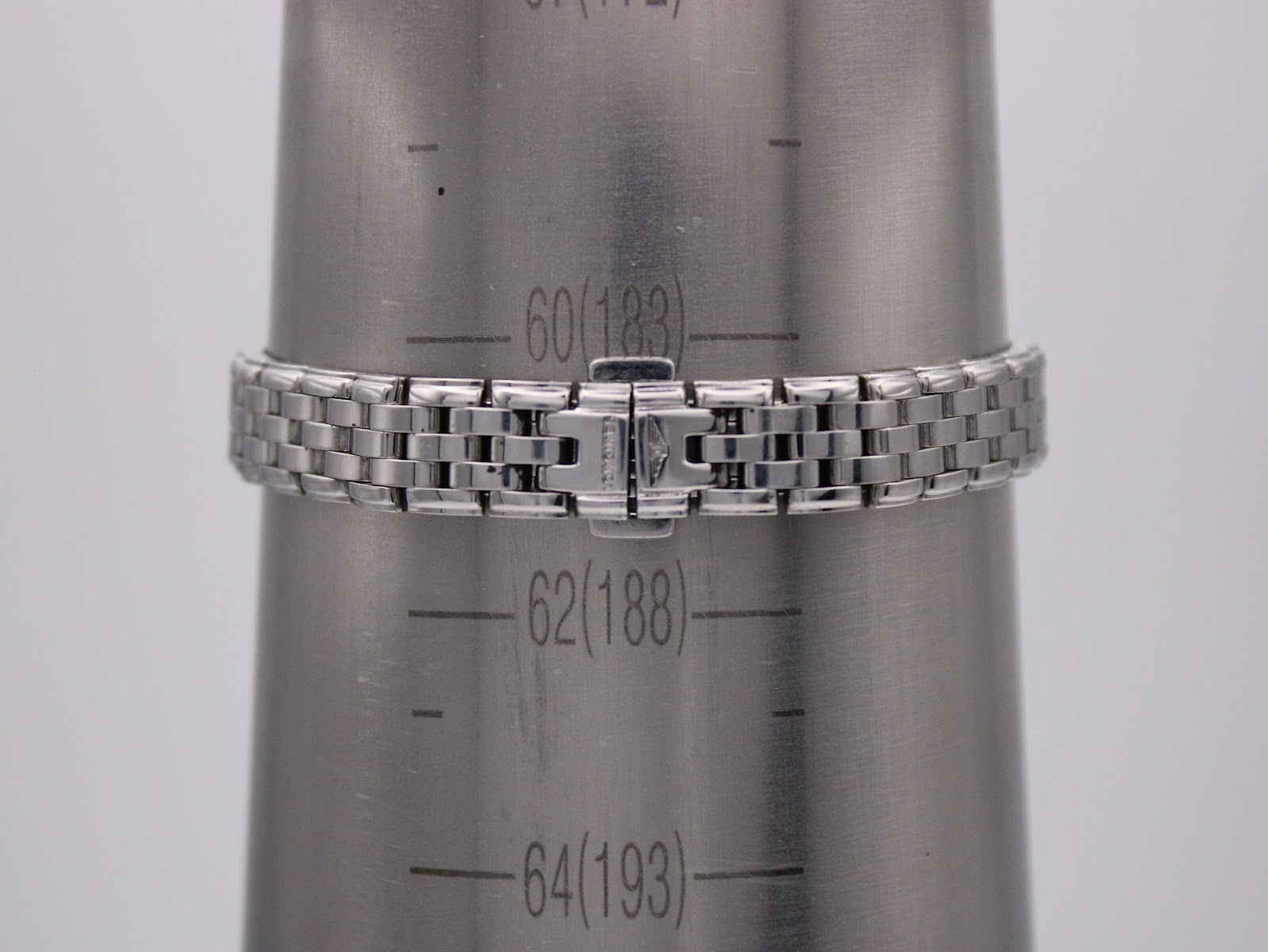 Close-up of the stainless steel bracelet and signed clasp on a wrist sizing cone, showing a wrist circumference of approximately 18.3cm.