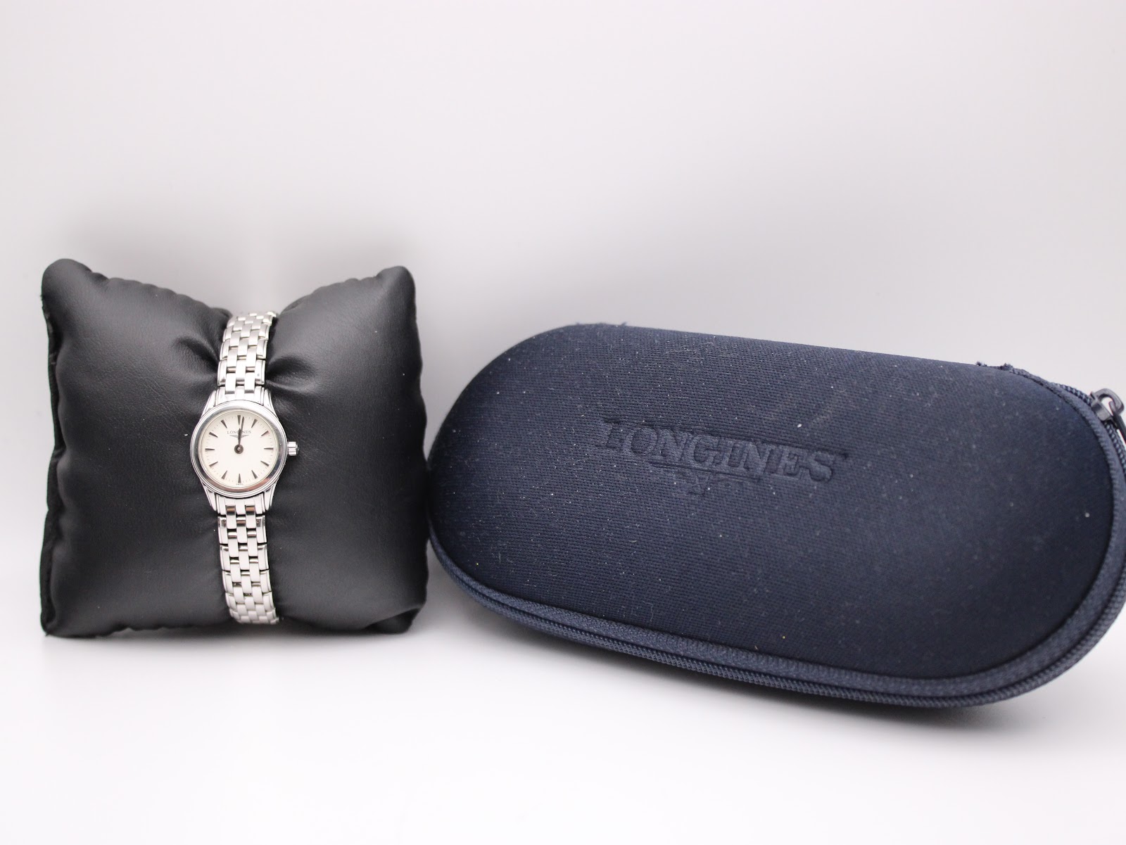 Longines L4.215.4 watch on a black cushion next to its original navy blue Longines travel case.