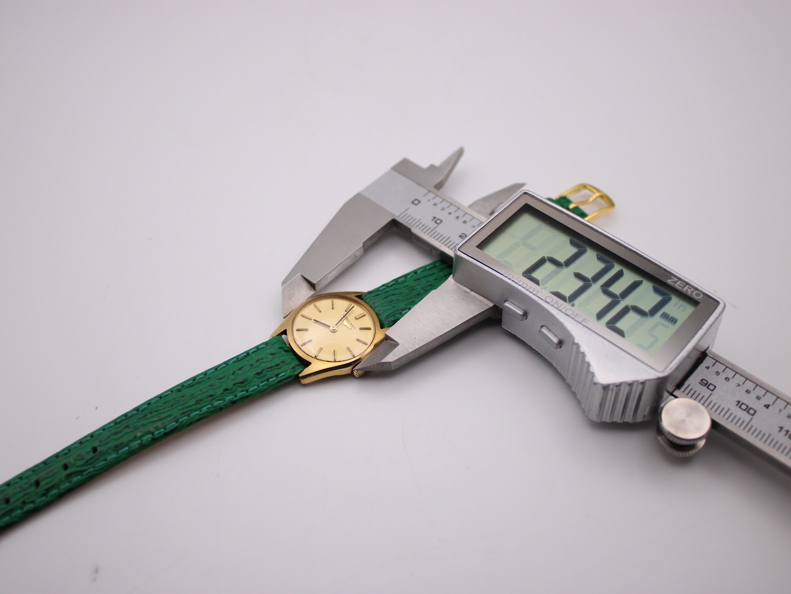 Close-up of the Longines watch being measured by a digital caliper, displaying a case diameter of 23.42mm.