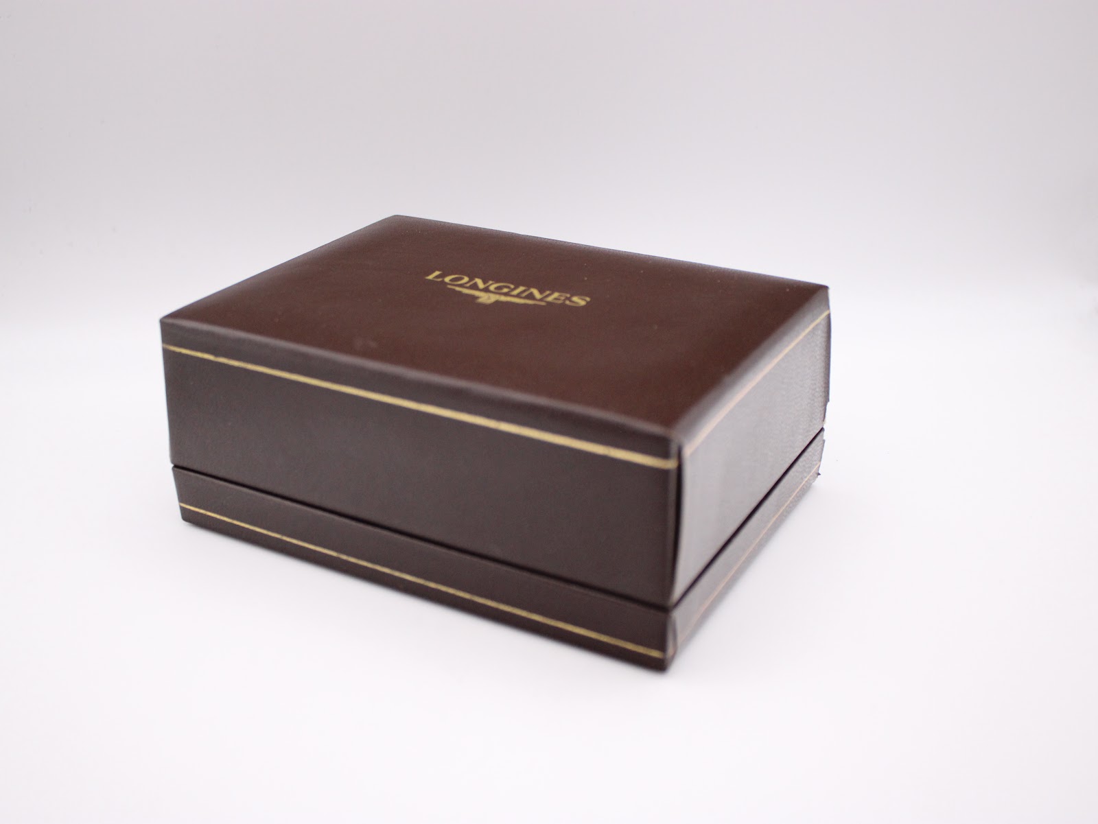 Closed view of the rectangular brown Longines presentation box with gold trim and the brand logo on the lid.