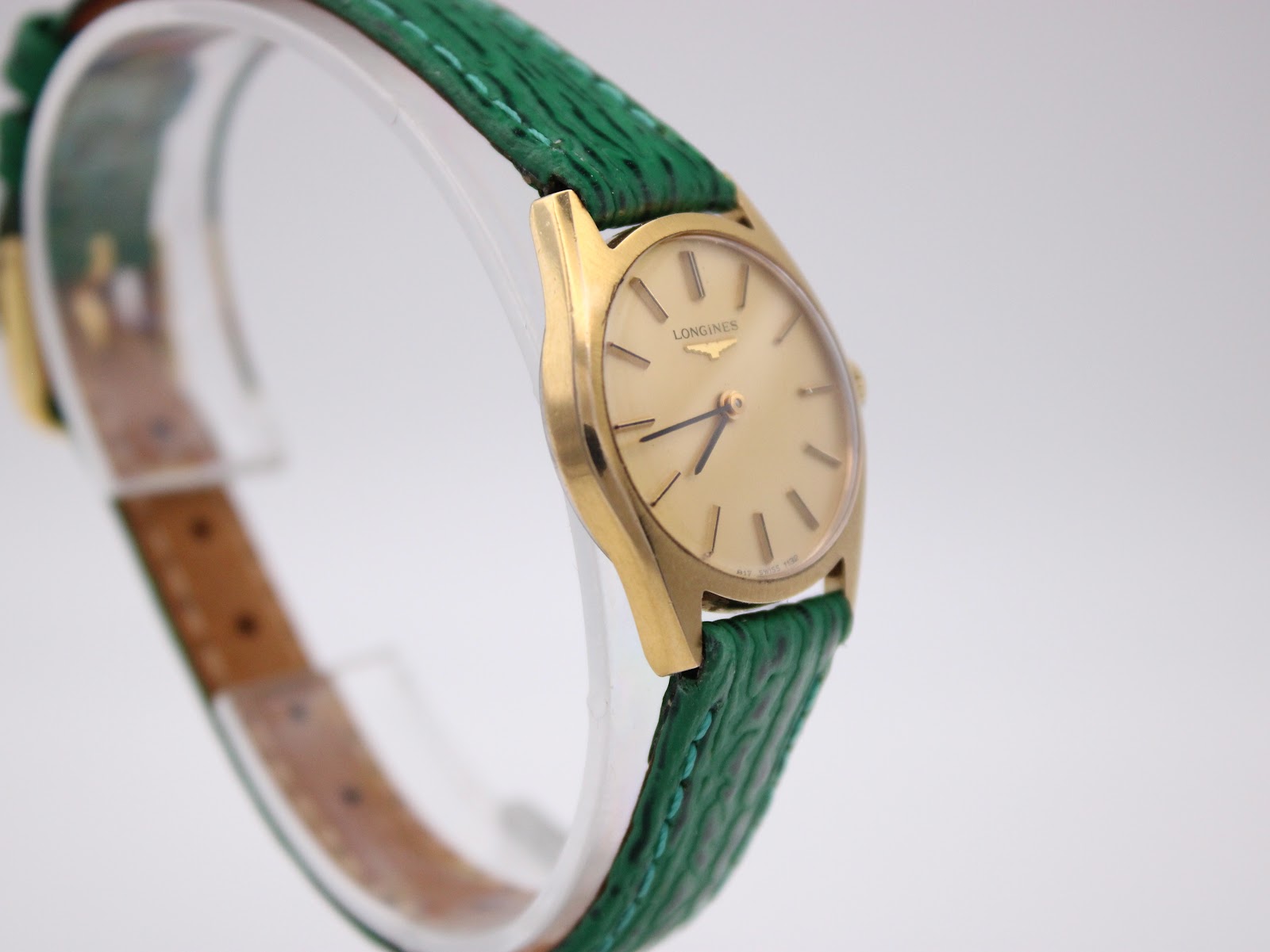 Another angled three-quarter view of the Longines watch on a clear stand, focusing on the dial and the green strap.