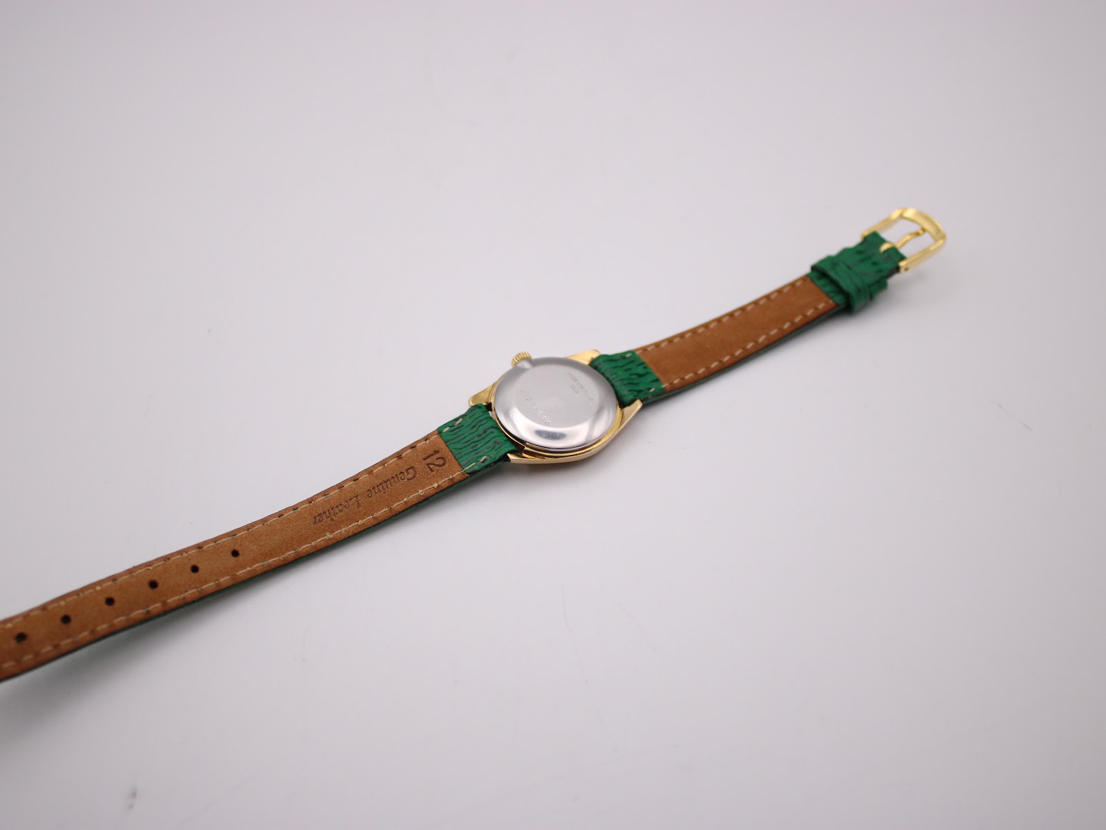 Back view of the Longines watch showing the stainless steel case back and the brown underside of the green leather strap, marked 'Genuine Leather'.
