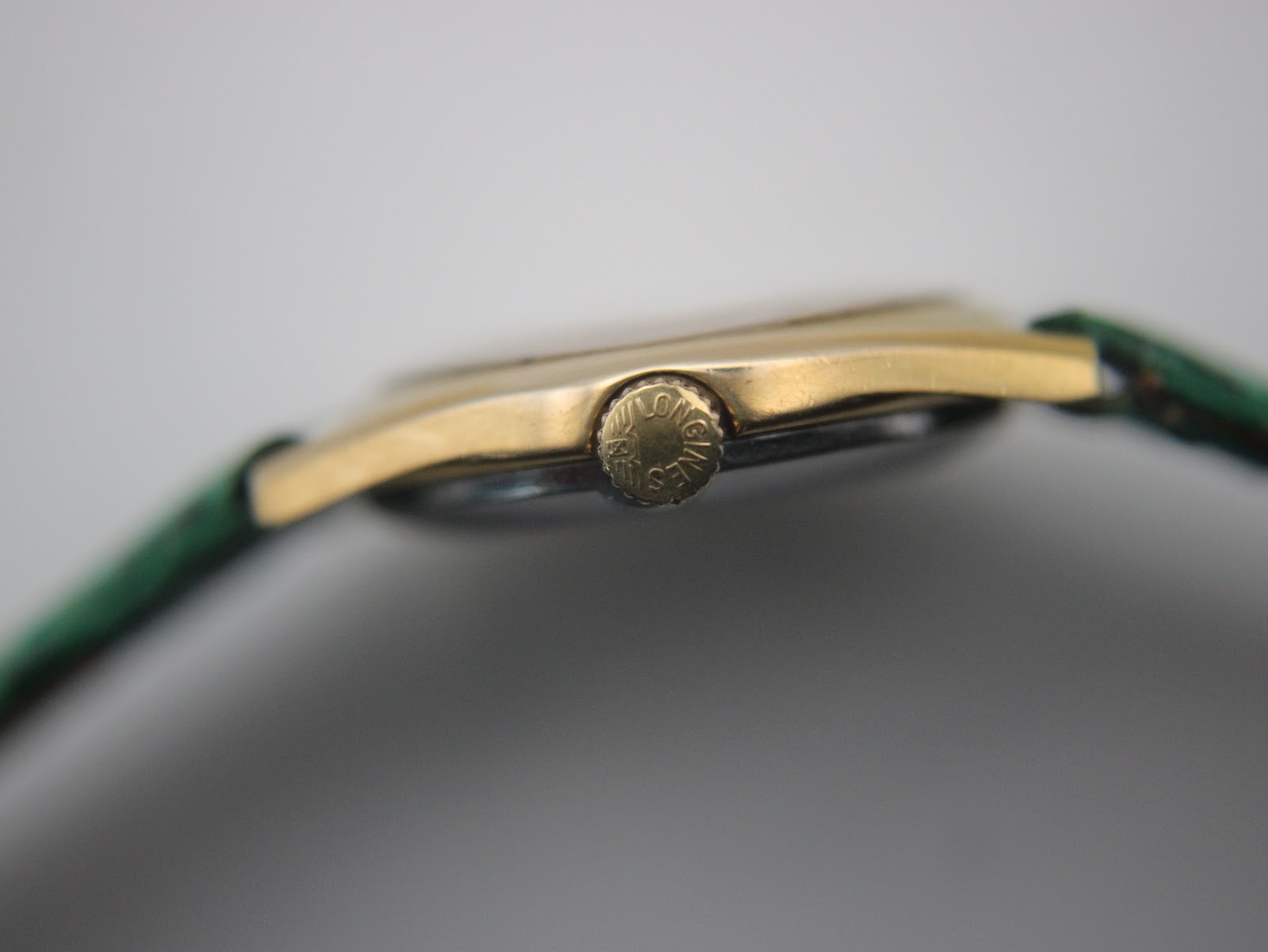 Close-up side view of the fluted gold-tone crown, clearly showing the embossed Longines winged hourglass logo.