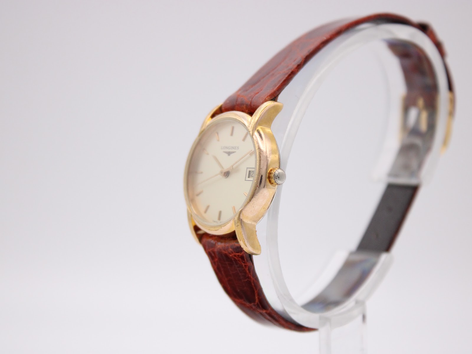 Angled side view of the Longines L4.197.2 watch, highlighting the gold case and brown strap on a watch stand.