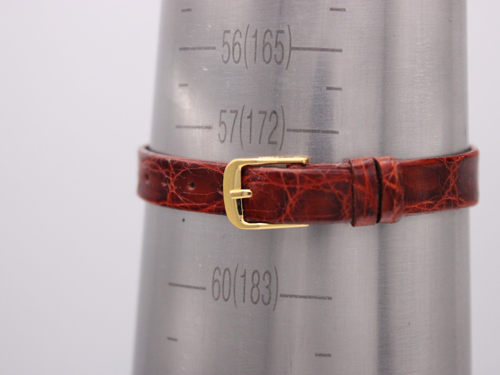 The brown leather strap fastened around a wrist sizing gauge, showing it fits approximately 172mm (57 units).