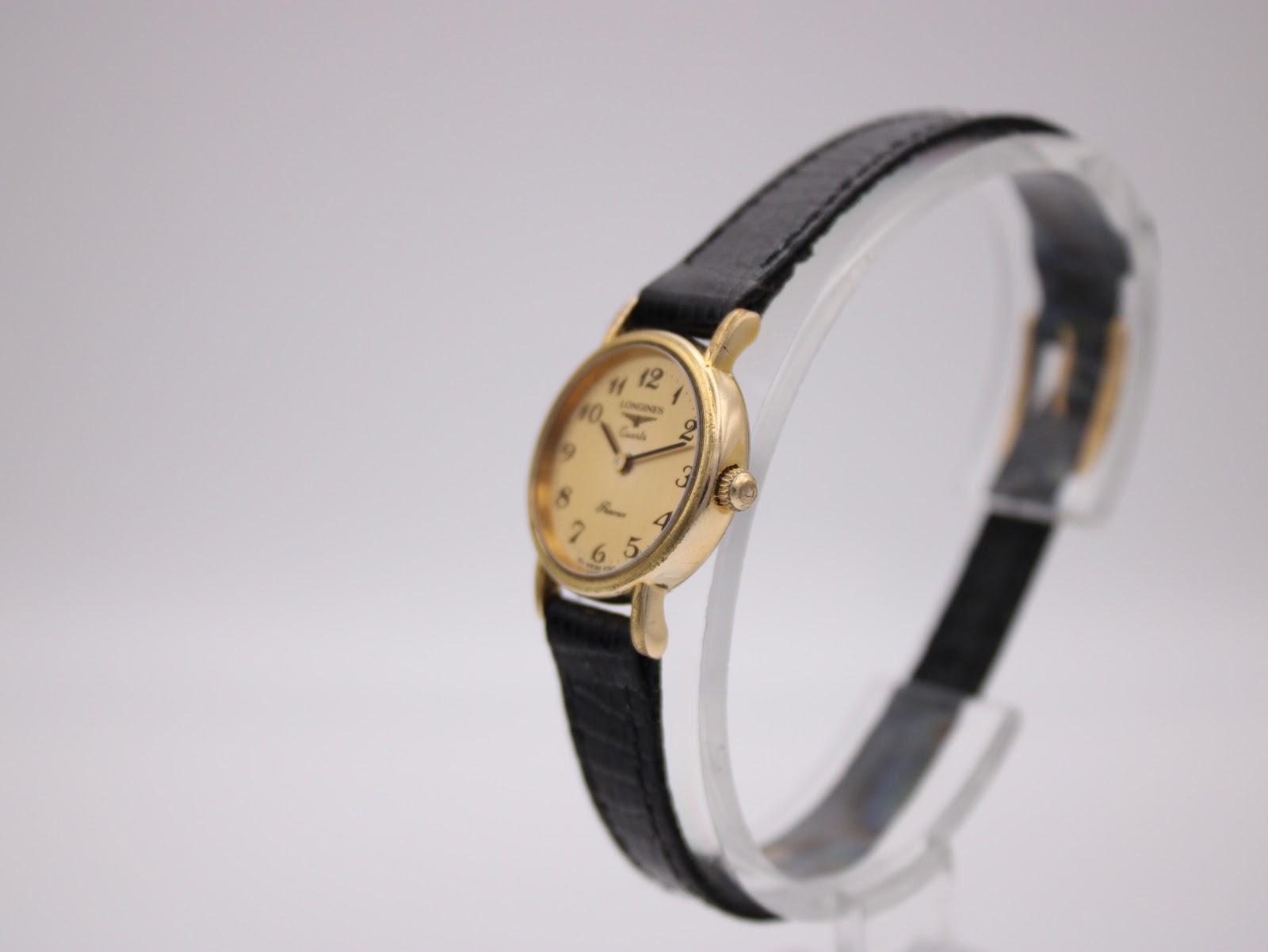 Angled side view of the Longines Presence watch on a stand, highlighting the gold-tone case and crown.