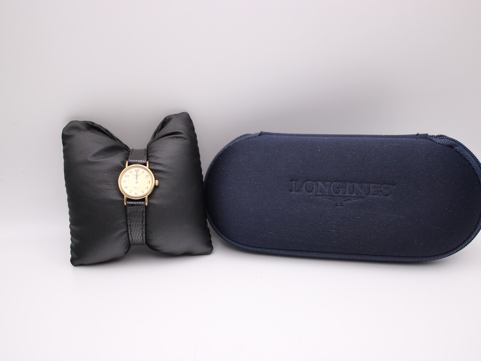 The Longines Presence watch resting on a black watch cushion next to its original dark blue Longines presentation box.