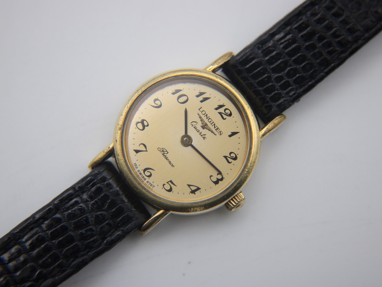 Close-up, top-down view of the watch dial, clearly showing "Longines Quartz Presence" text and Arabic numerals.