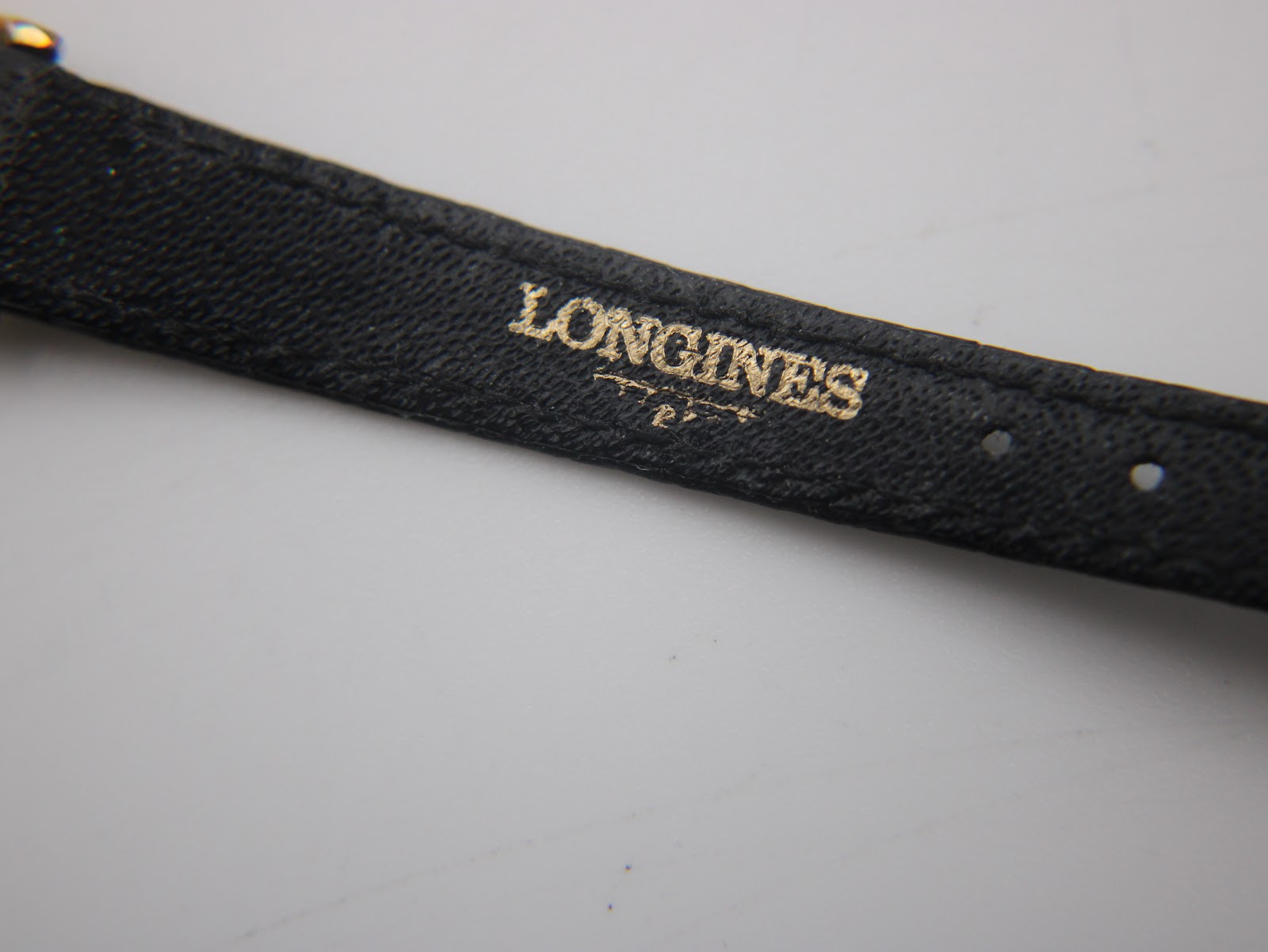 Close-up of the underside of the black leather strap showing the embossed "LONGINES" branding.