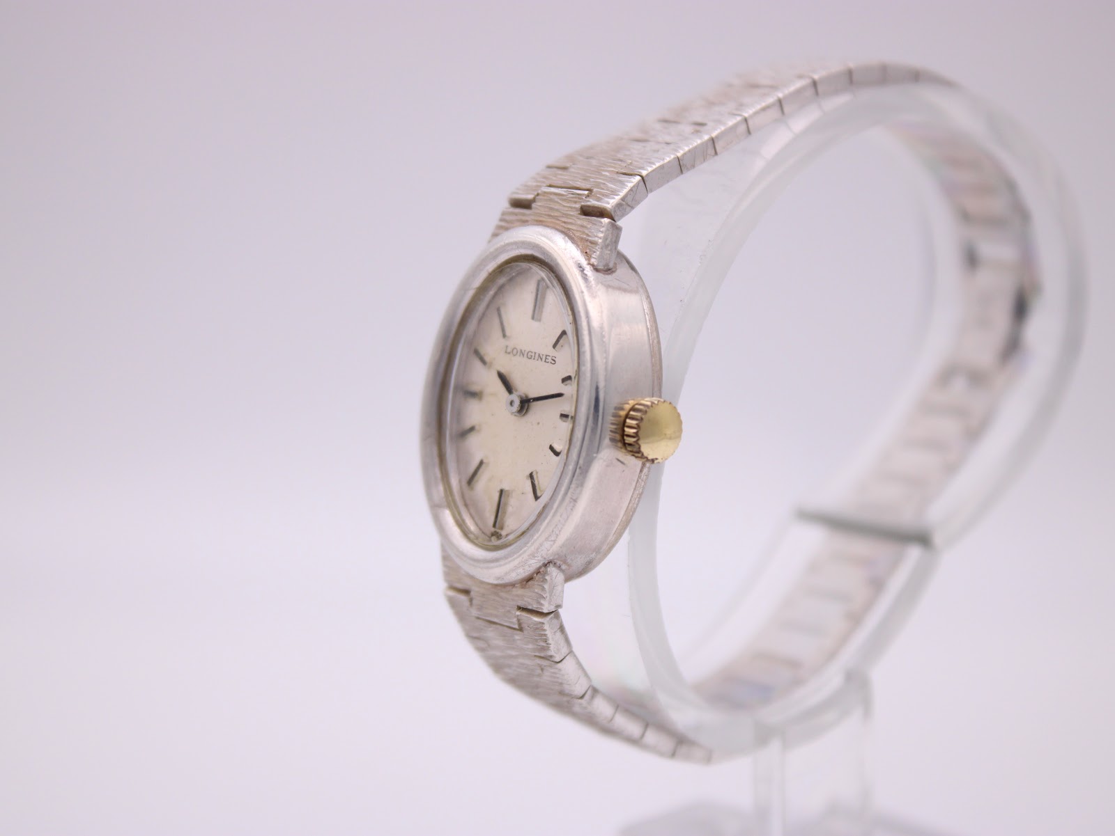 Side profile of the Longines 5601 watch, highlighting the oval sterling silver case, a small gold crown, and the textured bracelet.