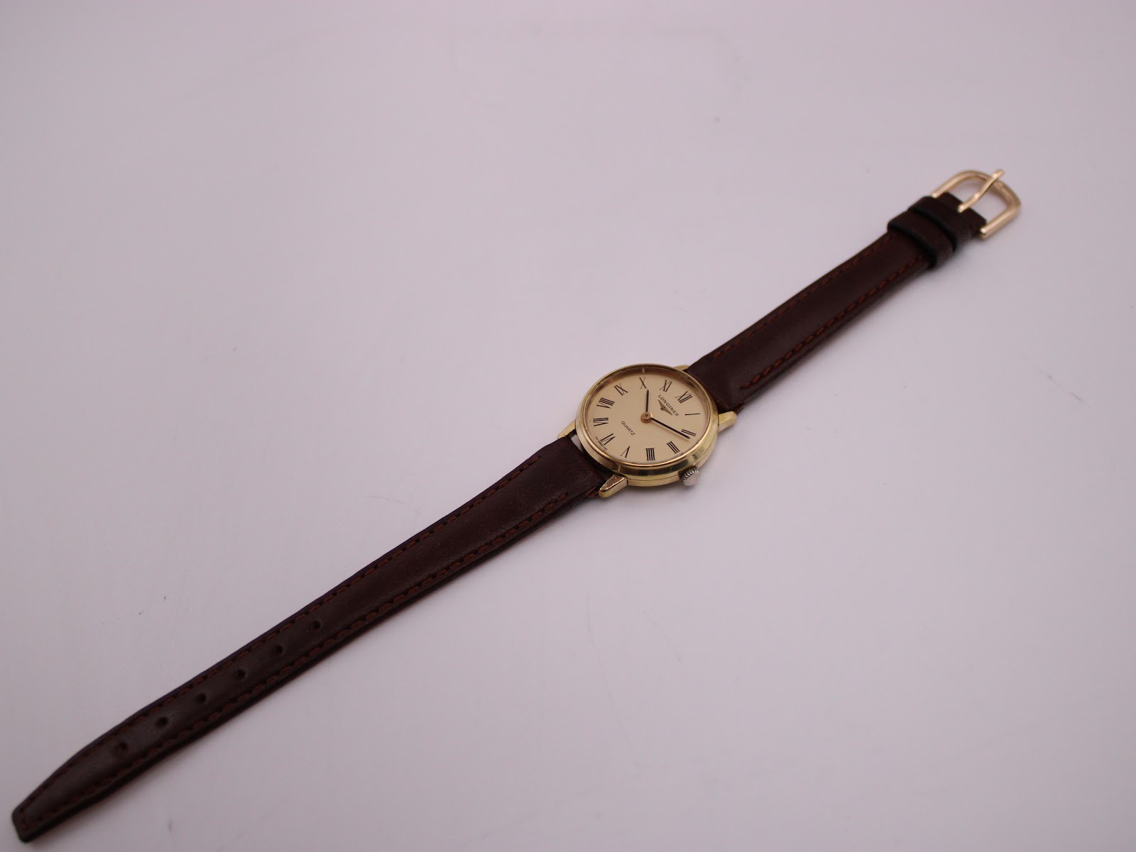 Full length view of the Longines watch with its brown leather strap extended, showing the gold buckle.