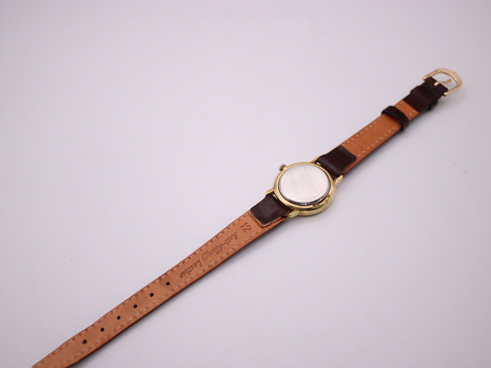 Top-down view of the Longines watch and strap, showing the stainless steel case back and the underside of the brown leather strap.