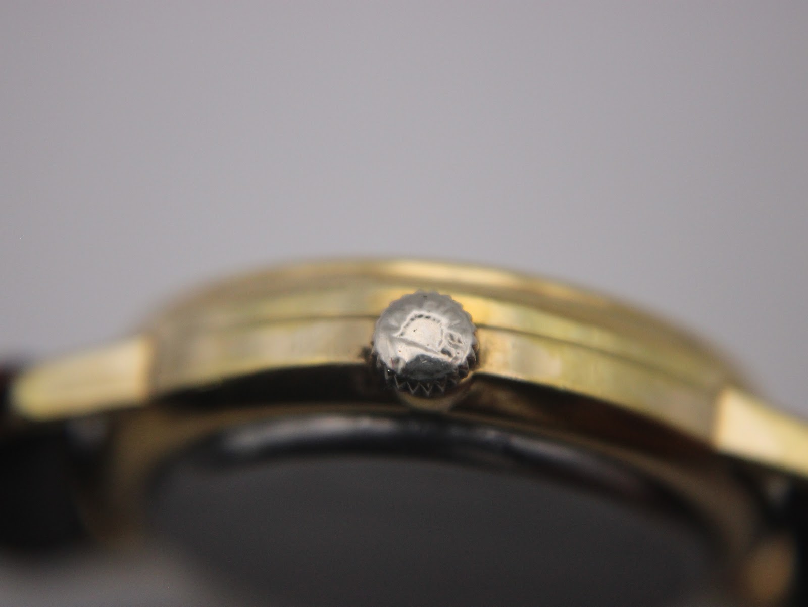 Extreme close-up of the Longines signed crown on the gold tone watch case.