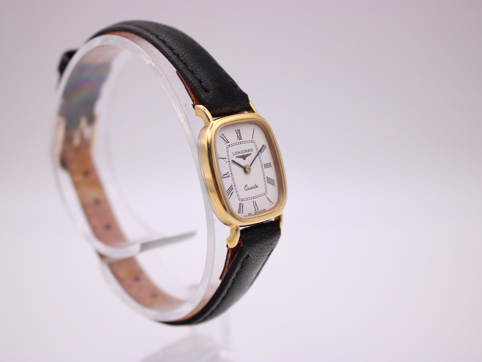 Angled front view of the Longines watch on a clear stand, highlighting the white dial and gold case.
