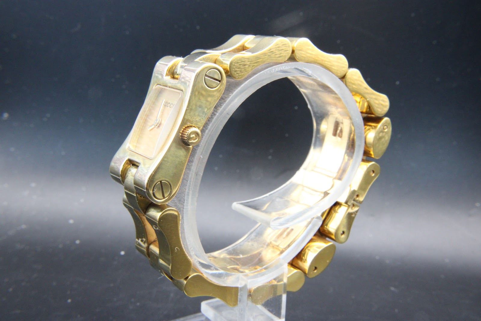 Back-left three-quarter view of the Gucci 2305L, showcasing the unique sculptural screw-link integrated gold-tone bracelet.