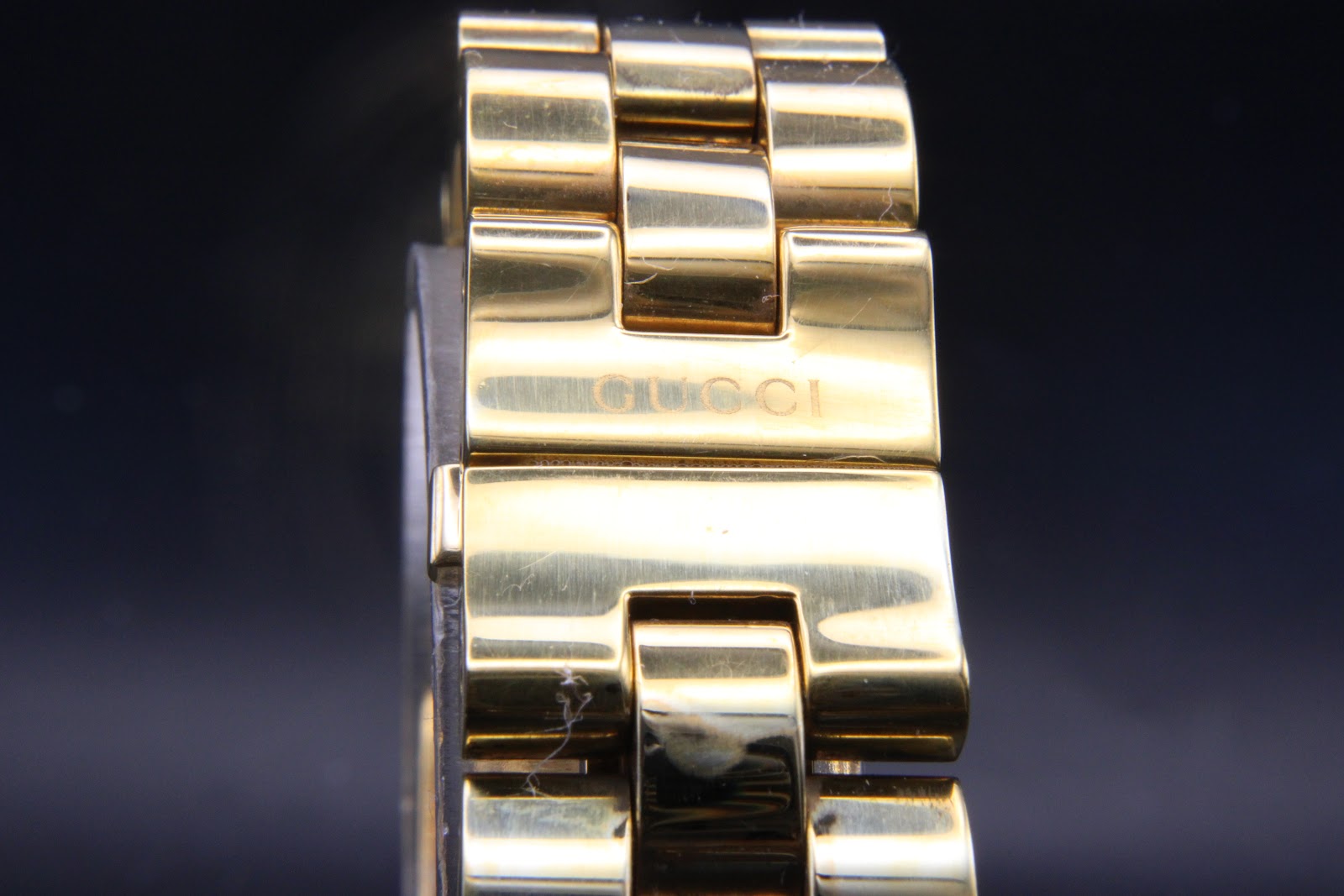 Close-up of the Gucci 2305L integrated bracelet's hidden deployant clasp area with etched 'GUCCI' signature.
