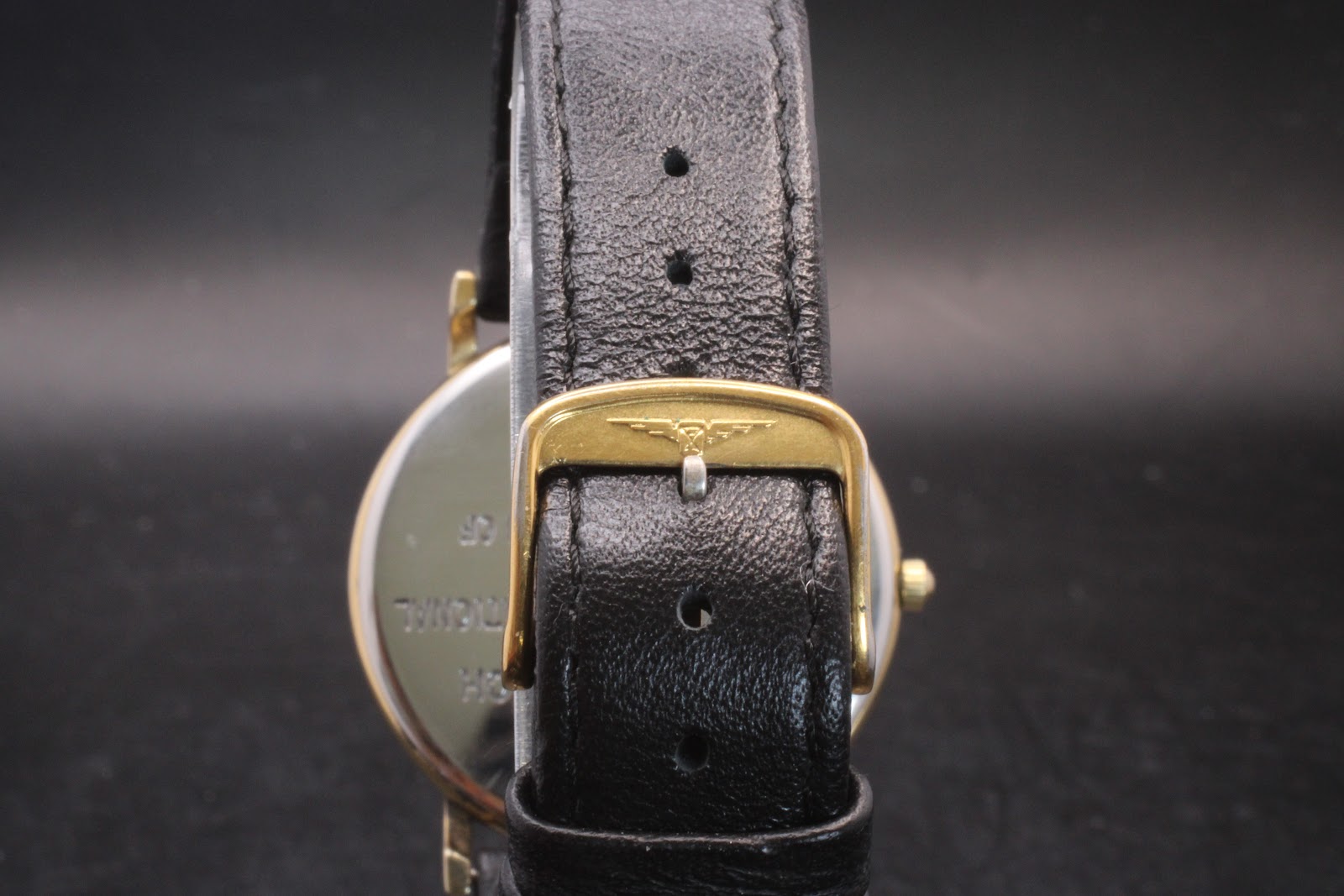 Close-up of the original Longines signed gold-tone buckle on the black leather watch strap.