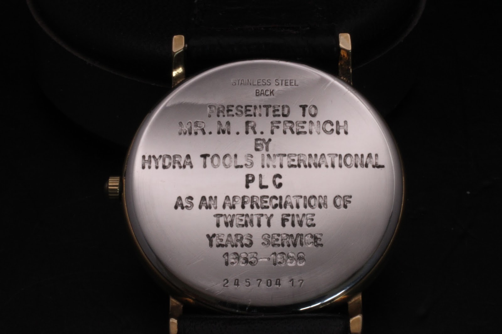 Close-up of the stainless steel case back, showing the dedication engraving from Hydra Tools International PLC and the watch serial number.