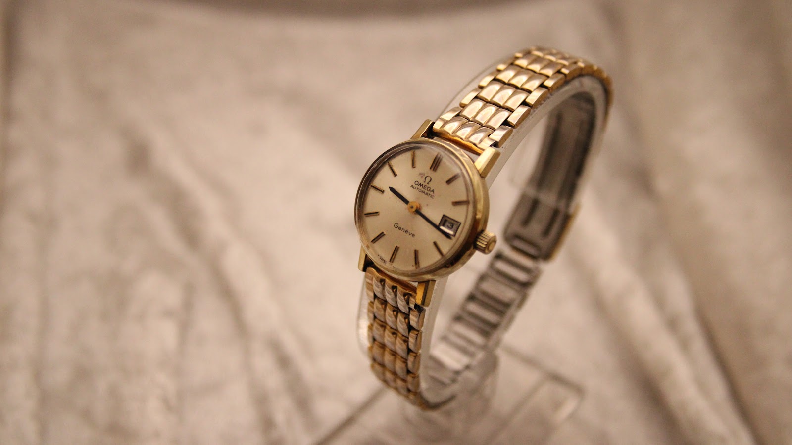 Three-quarter view of the Omega Geneve watch on a clear display stand, showing the dial and bracelet.
