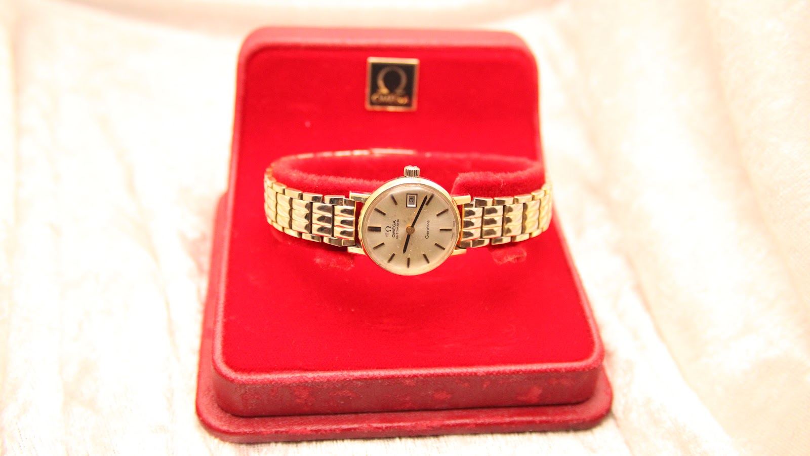 Front view of the Omega Geneve watch presented in its original red Omega branded box.
