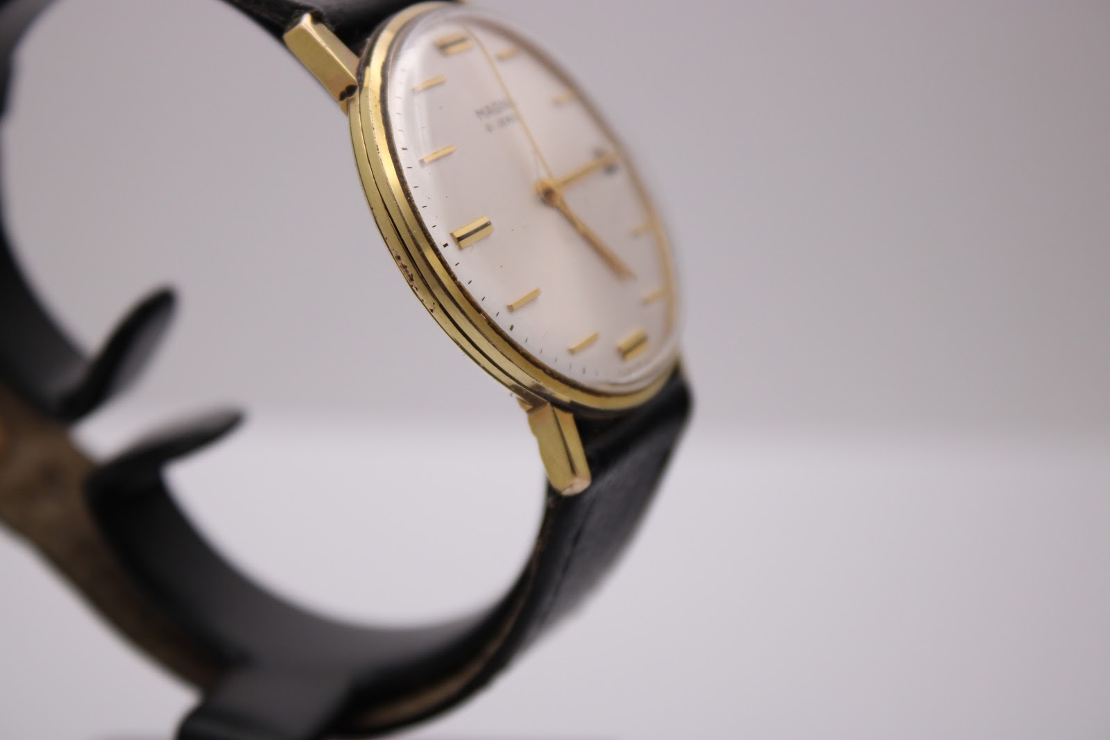 Another angled side view of the Magna watch, focusing on the left side of the gold-tone case and lug area.
