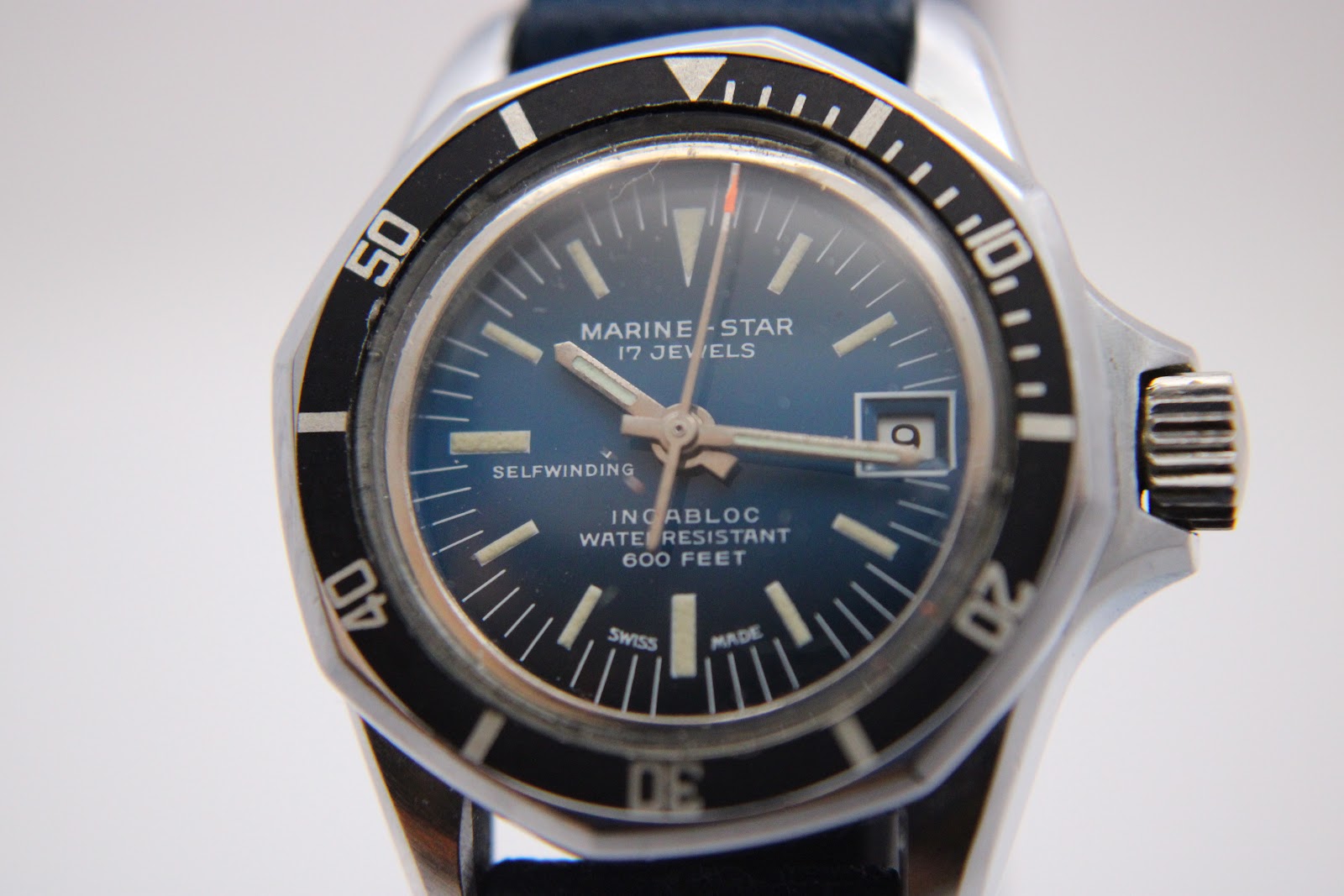 Close-up of the Marine Star blue sunburst dial, featuring luminous indices, hands, date window, and "600 FEET" water resistance text.