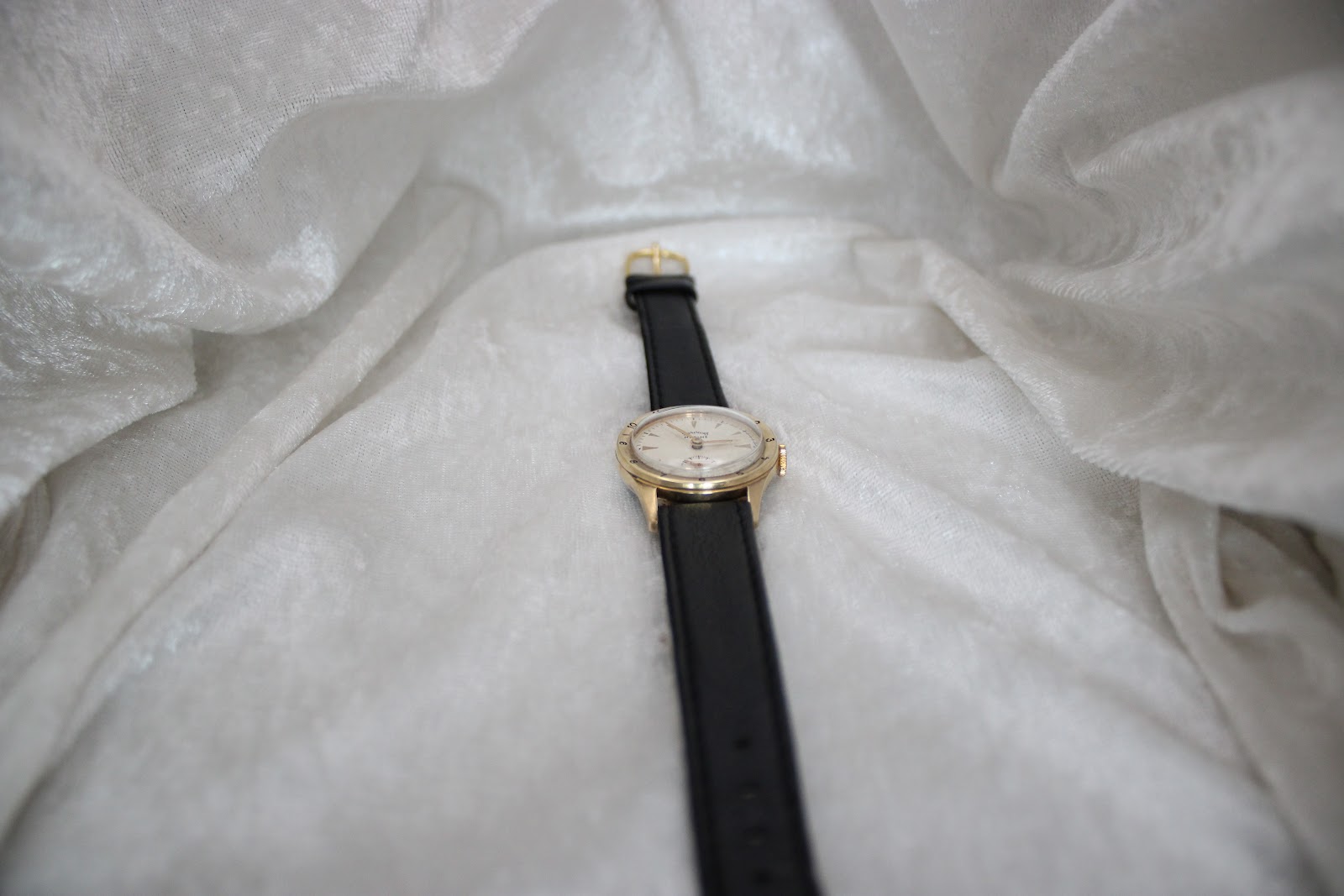 Full overhead shot of the Services Marine watch with its black leather strap laid flat on a textured white fabric background.