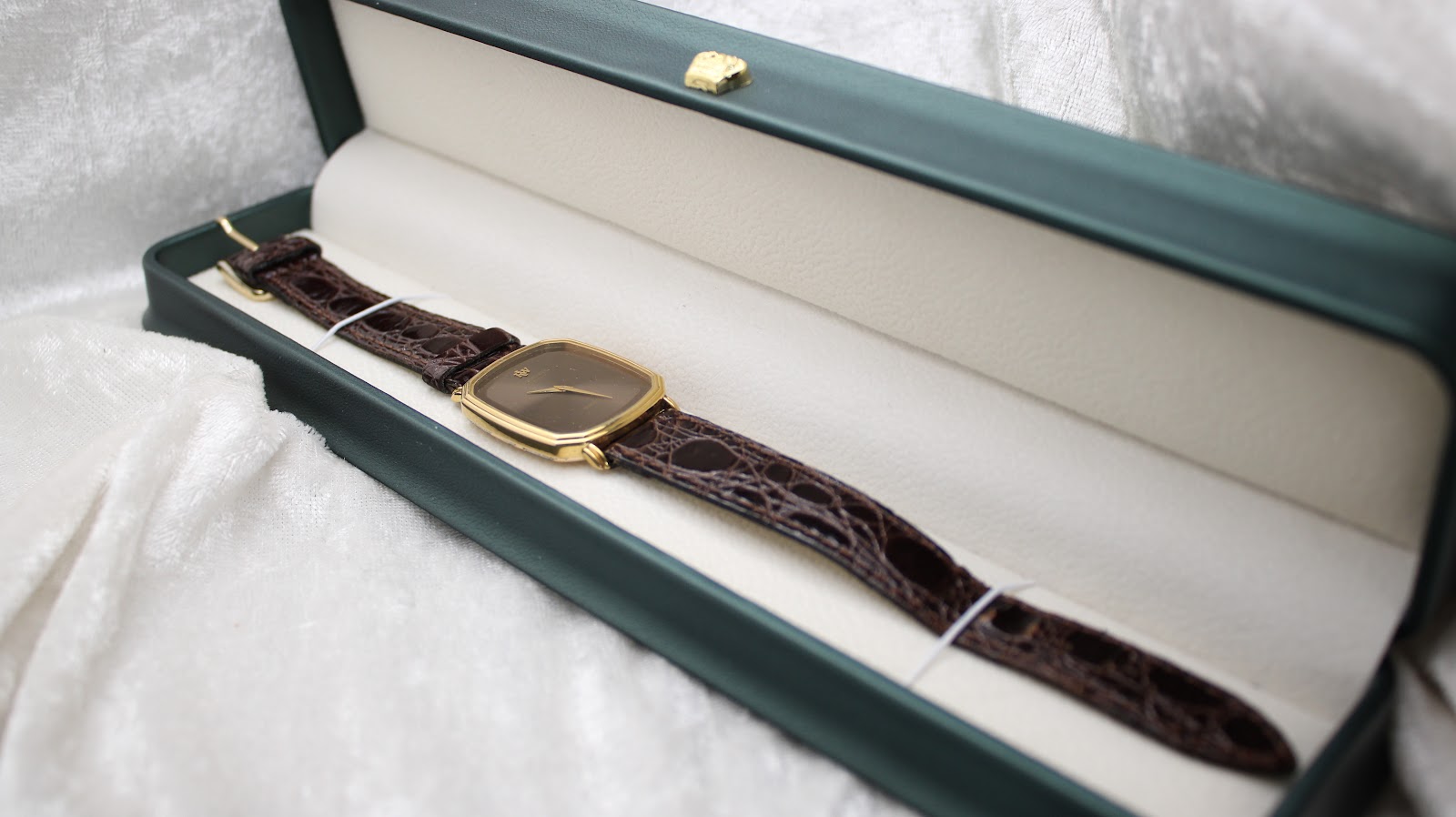 The Raymond Weil watch neatly displayed inside a dark green presentation box with white interior lining.