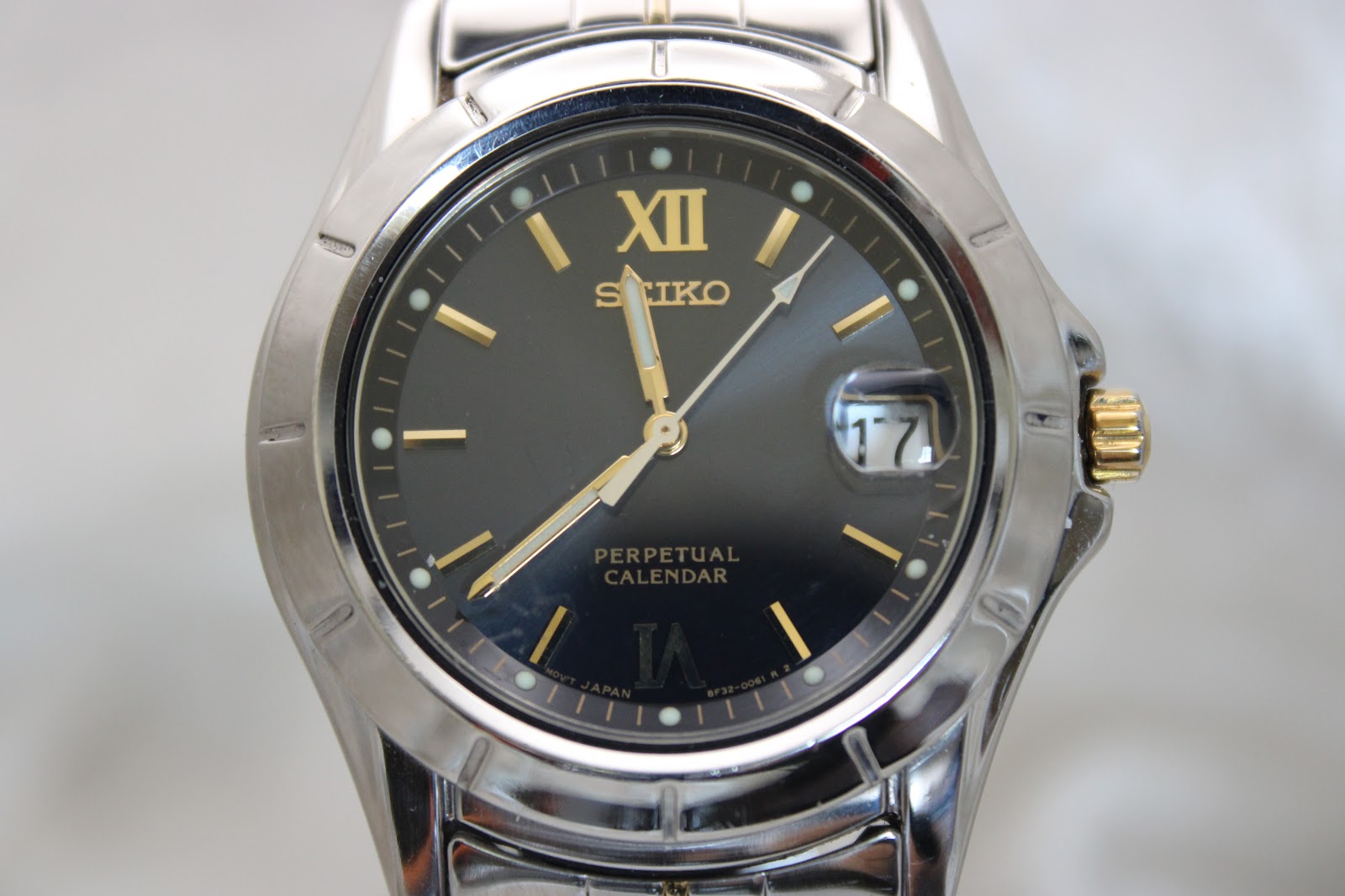 Close-up front view of the Seiko perpetual calendar black dial with gold Roman XII, baton indices, date magnifier, and luminous hands.