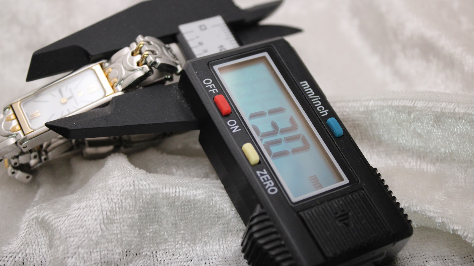 Digital caliper measuring the watch case, displaying a width of 13.30 mm, with the watch resting on a white textured background.