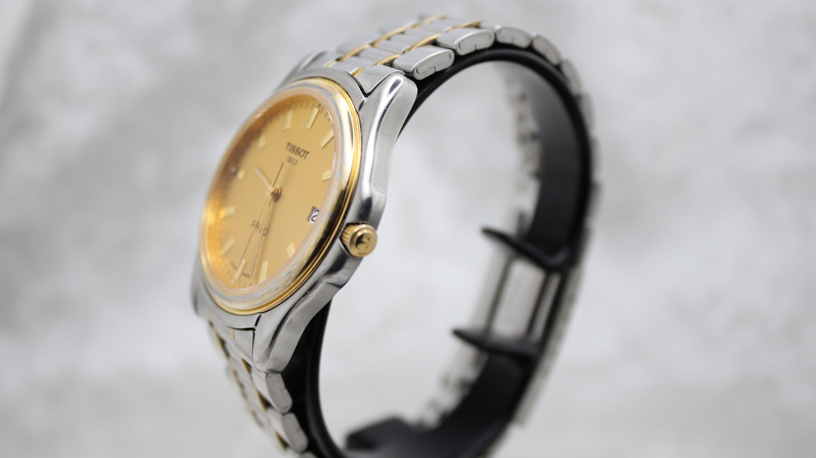Angled view of the Tissot PR 50 watch on a black display stand, showcasing its two-tone case and bracelet from the right side.