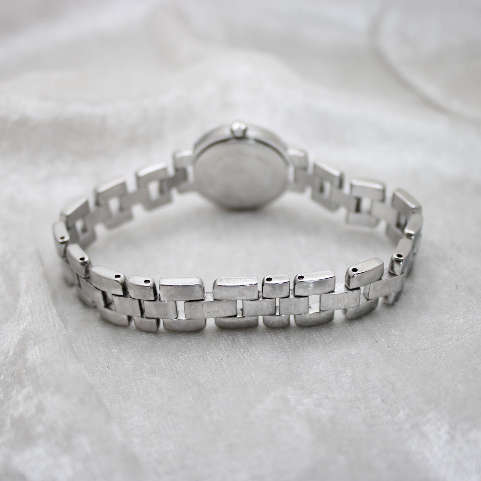 Rear view of the Tissot G330's integrated stainless steel bracelet, laid on a white textured surface.