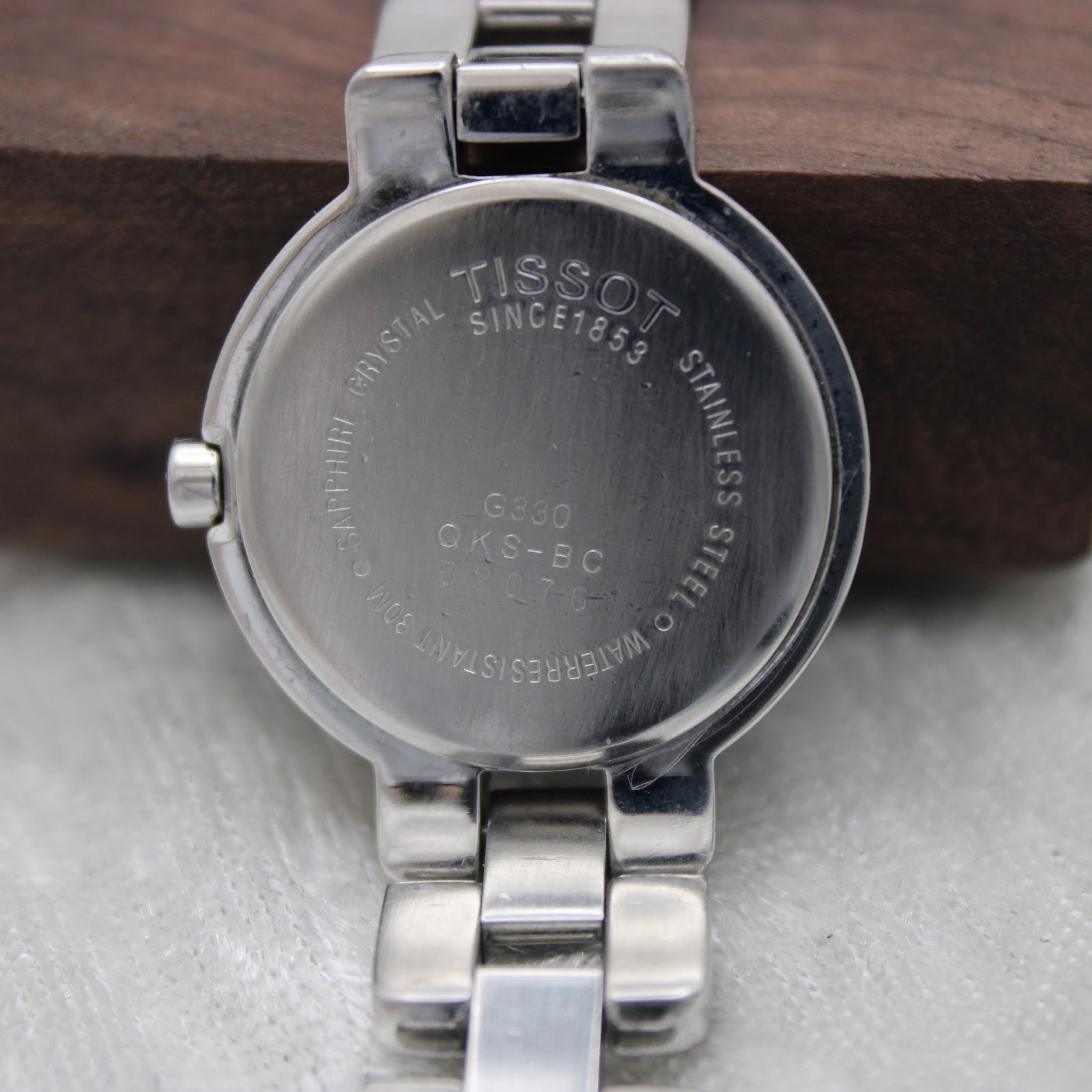 Detailed view of the Tissot G330 watch case back, engraved with "TISSOT SINCE 1853", model G330 QKS-BC, and water resistance information.
